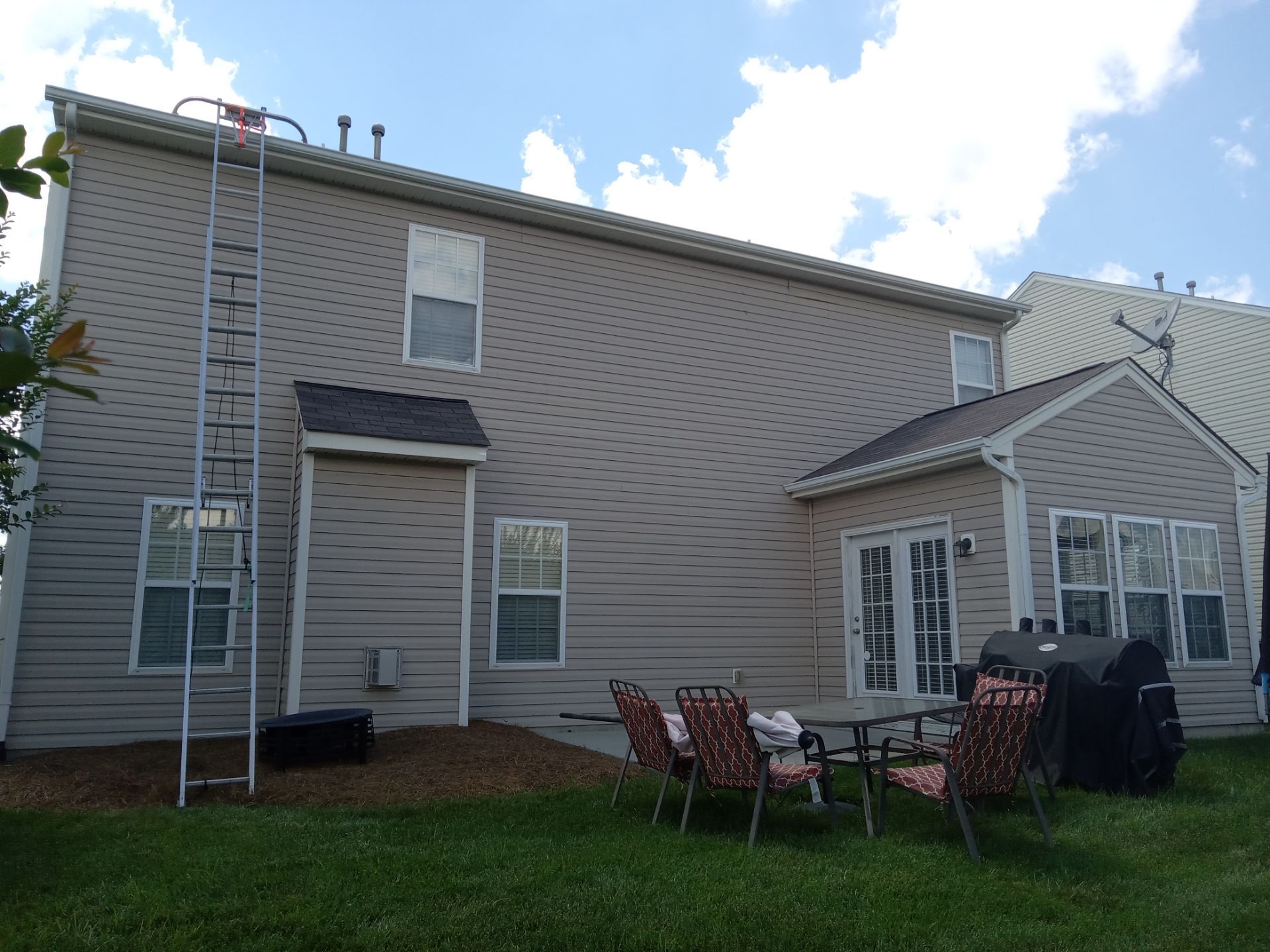 the image shows the exterior of a two-story residential house a pressure washing company is likely providing cleaning services for the siding of the house the presence of a ladder suggests that workers will clean higher areas that are not easily reachable from the ground the services may also include washing the outside of the windows and cleaning other exterior features such as the gutters soffits and downspouts the equipment and technique applied would ensure the removal of dirt grime mold and other build-ups to restore the appearance of the home's exterior surfaces