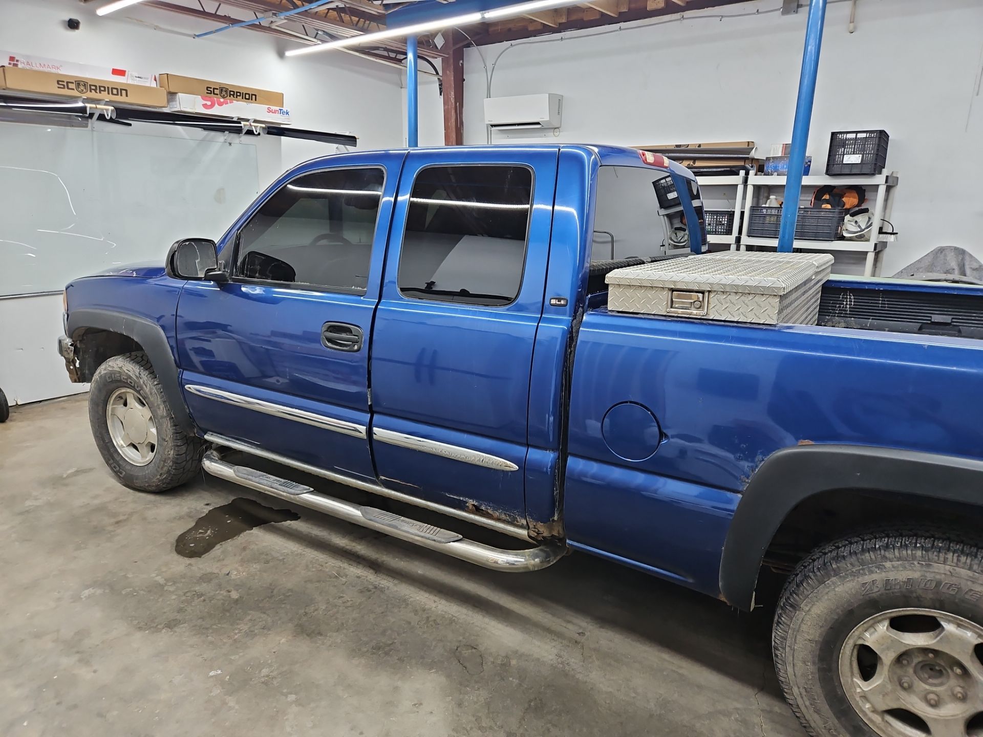 the service being performed is window tinting on a blue pickup truck the windows have a dark film applied to them to reduce glare and heat inside the vehicle it enhances privacy and gives the truck a sleek appearance the process involves cleaning the glass thoroughly before applying the tint for a smooth finish the vehicle appears to be in a shop environment where professional tinting services are conducted