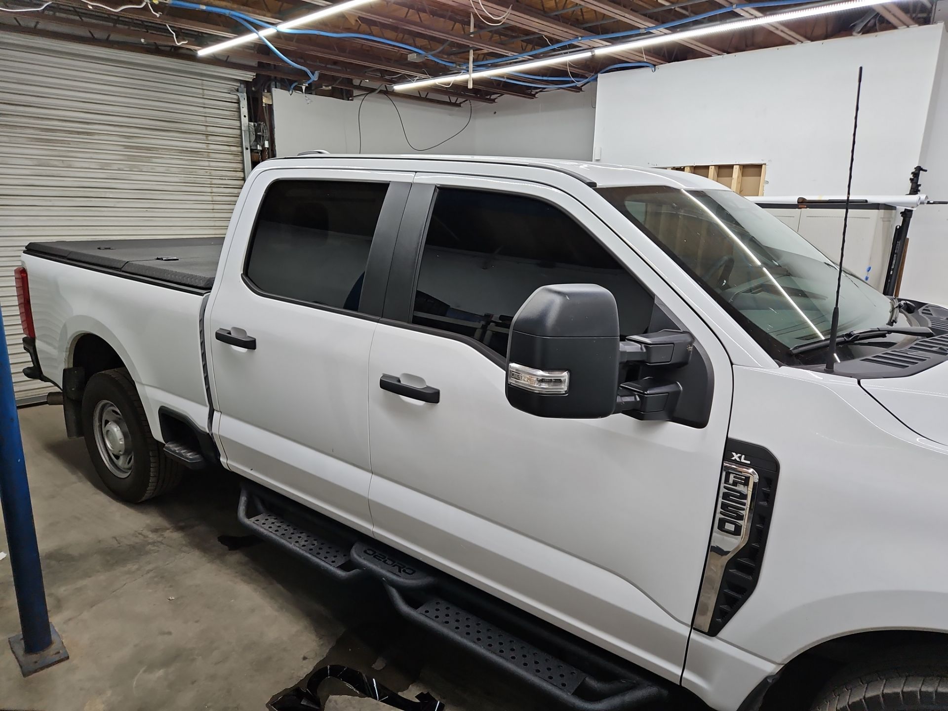 the service being done is the application of window tinting on a white pickup truck the windows are being tinted to enhance privacy reduce glare and provide protection from harmful uv rays the rear and side windows appear to have already been tinted while the front windshield may also be treated the overall process involves cleaning the glass to ensure a smooth application of the tint film