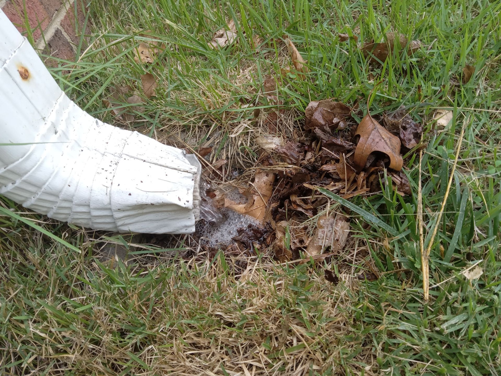 pressure washing company cleaning a white downspout and the ground area around it removing dirt and debris