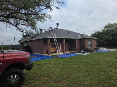 Workers removing old asphalt shingle roof on brick home.