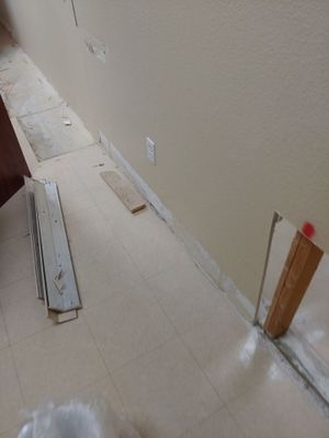 Lower wall area with baseboard removed, exposed trim pieces, and materials on the tile floor.