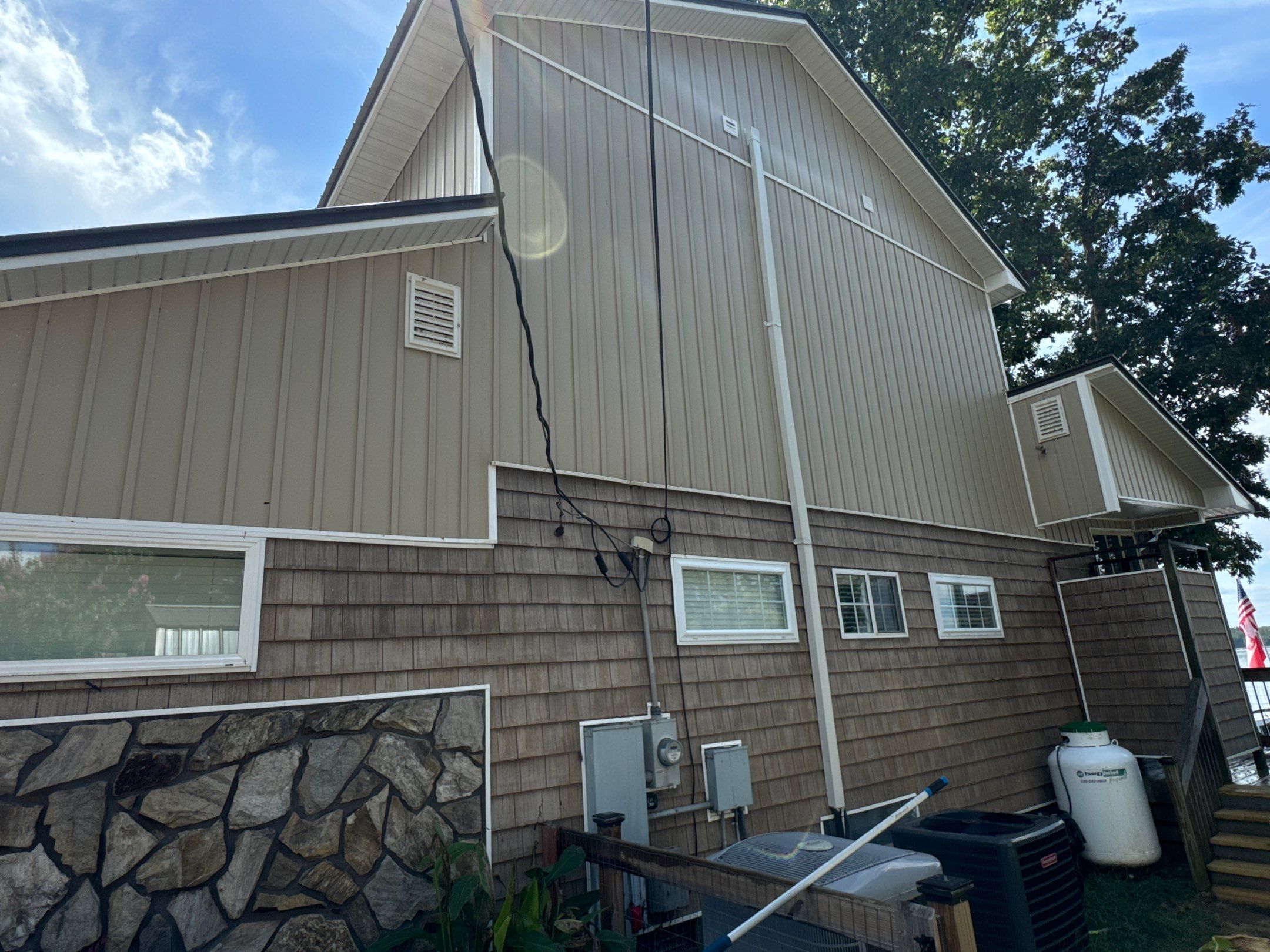 the service shown is cleaning the exterior walls of a house including siding and stone surfaces with a pressure washer