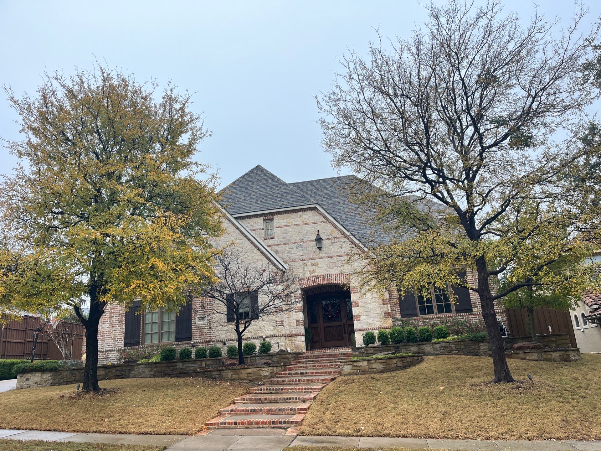 Light red brick/cream stone/espresso shutters with IKO Cornerstone by Tejas Roofworks + Restoration