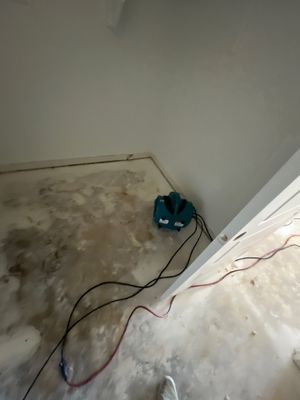 Small air mover and cords placed in the corner of a room with a concrete floor.