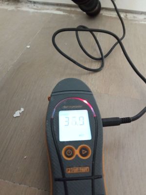 A digital moisture meter placed on hard surface flooring with a reading displayed on the screen.