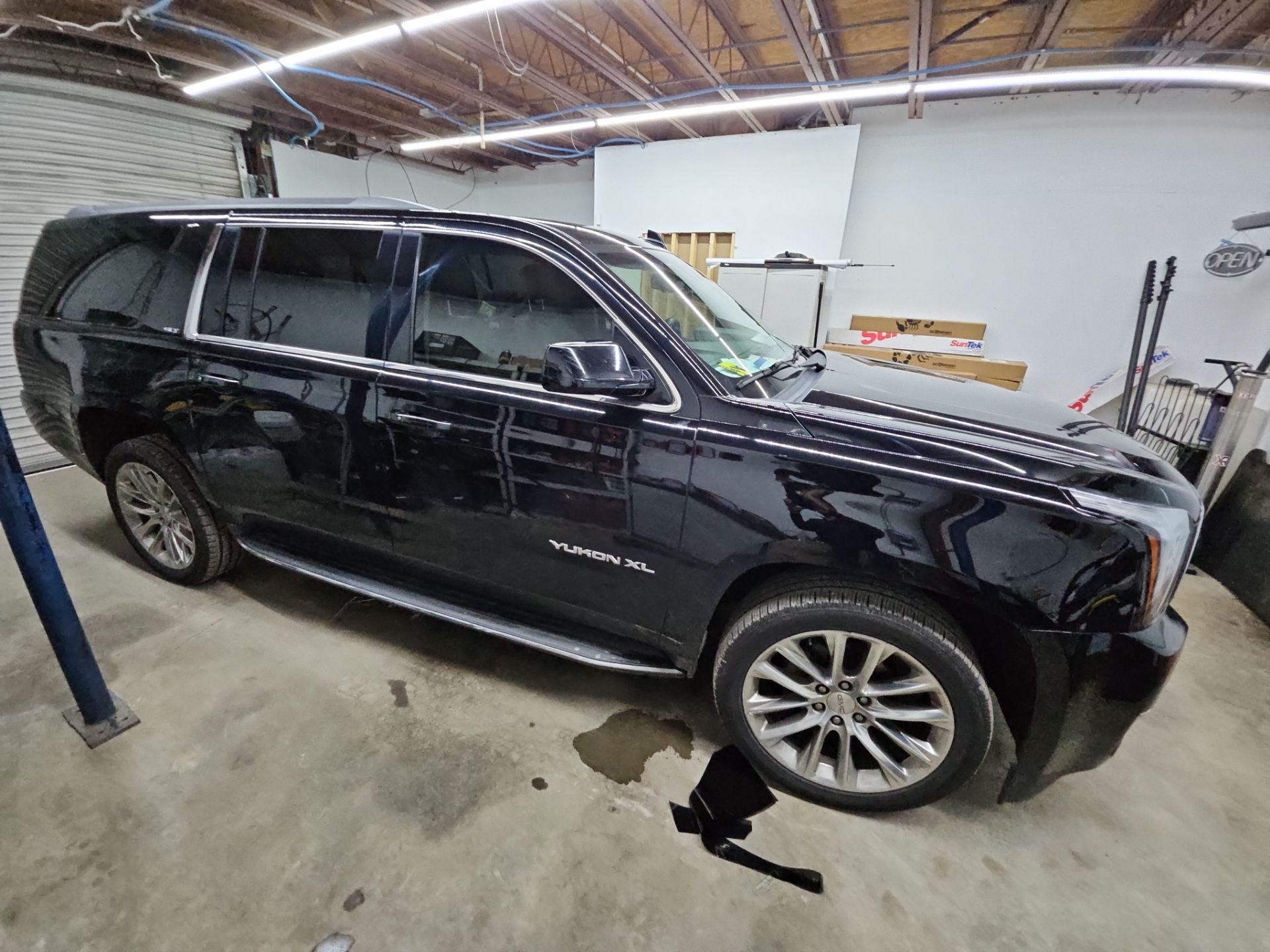 the image shows a large black suv that is likely undergoing window tinting services the vehicle is a yukon xl which has multiple windows being treated for tint the tinting process appears to be focused on enhancing privacy and reducing glare the vehicle is inside a workshop which indicates careful and professional installation the cleaned surfaces are ready for the application of window film to improve comfort and appearance