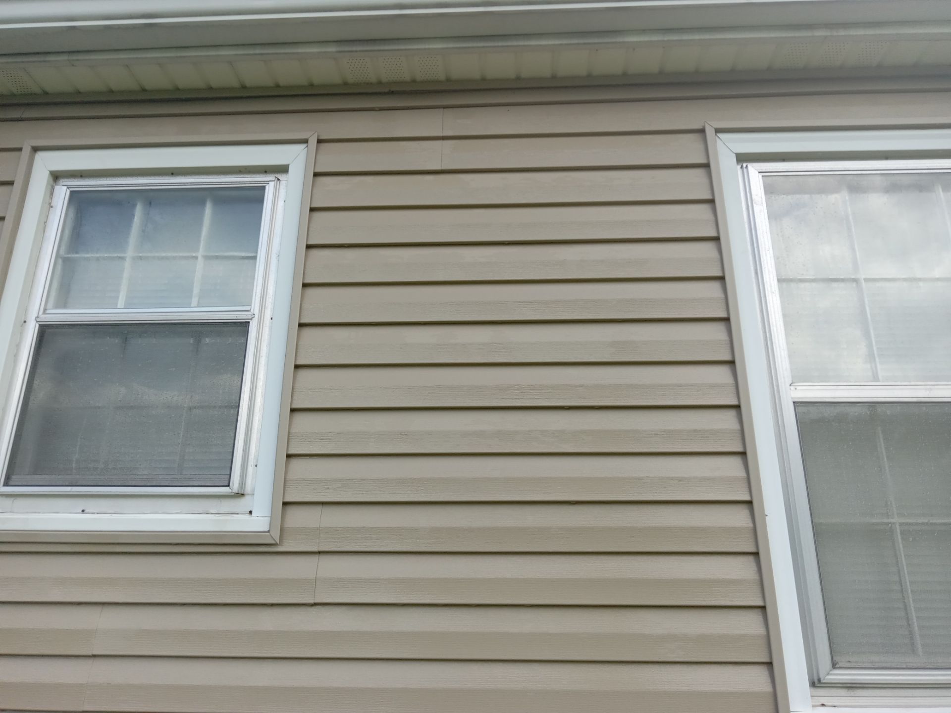 in the photo a pressure washing company is cleaning the exterior siding of a house the service includes washing the vinyl siding to remove dirt grime and possibly mildew or algae buildup the cleaning helps to restore the appearance of the house by making the siding look cleaner and more maintained the windows are closed to prevent water from entering the house and the area around the windows is also being cleaned to ensure a uniform cleanliness across the facade