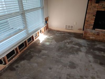 Living room with lower wall sections removed beneath windows and staining on the floor near a brick fireplace.