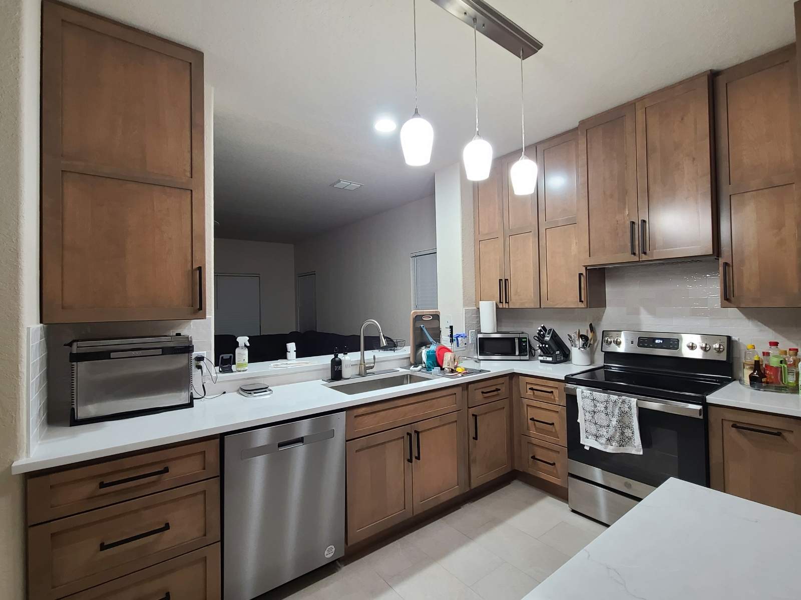 The old kitchen had a traditional builder-grade look with heavier wood cabinetry and busier finishes, while the new kitchen has a warm transitional design with cleaner lines, a brighter palette, and a more open, modern layout by Mena stone surfaces