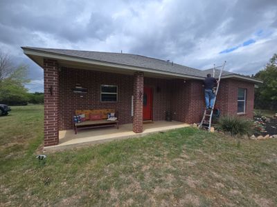 Worker on ladder installing asphalt shingle roof on brick home