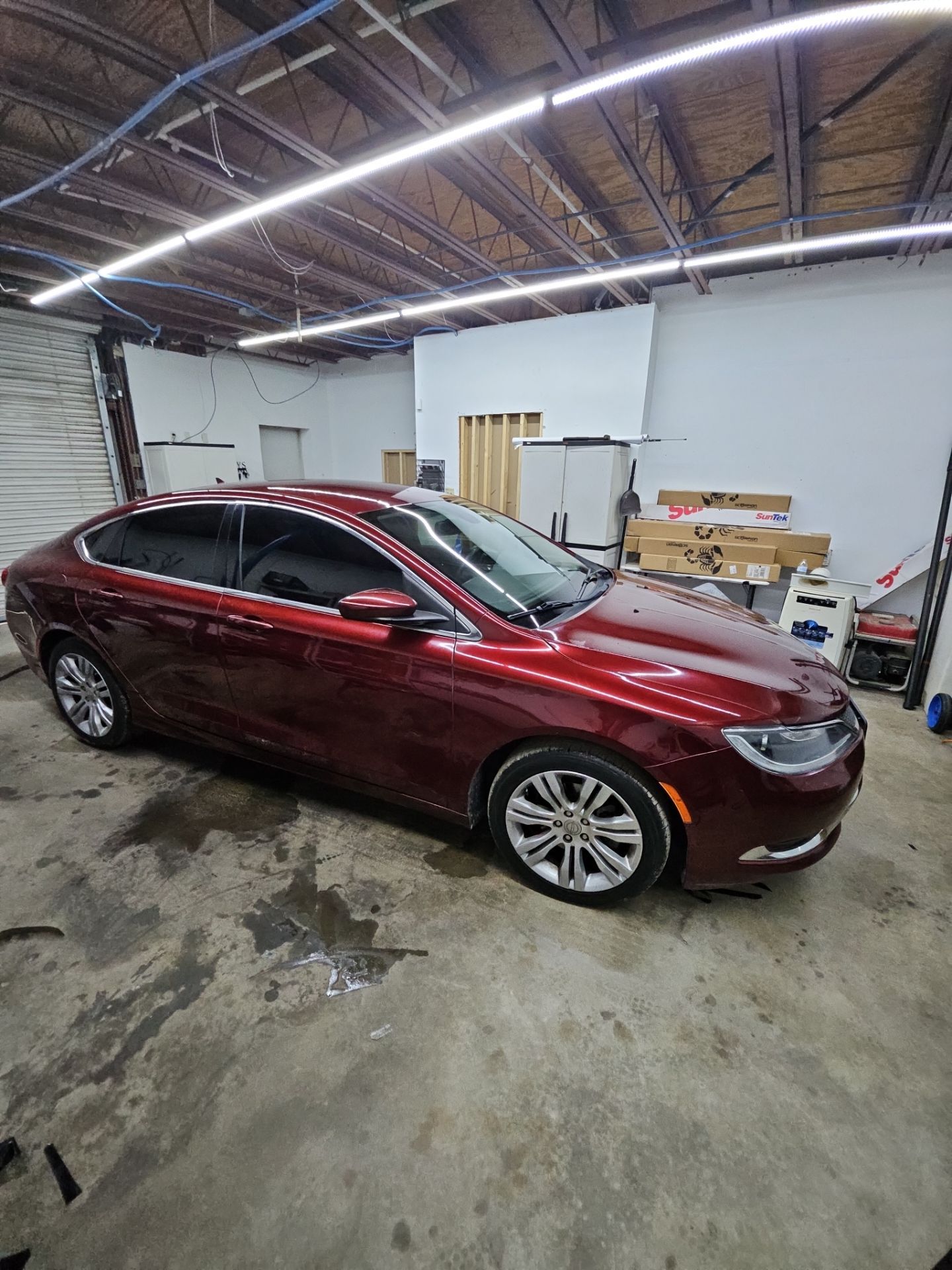 the service being performed is window tinting for the red car which has already been tinted the windows appear dark and clean indicating a professional installation the car is likely being prepared or checked for any final details after the tinting process the workspace looks organized with proper lighting and equipment visible around the vehicle