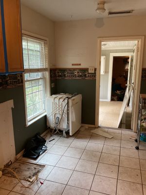 Kitchen area with tile flooring, windows, wall openings, removed fixtures, and appliances moved from their usual positions.