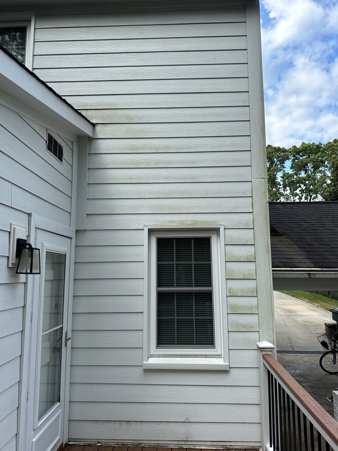 pressure washing company is cleaning exterior siding with visible mold and stains on white wooden surfaces of a house