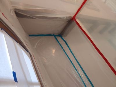 Clear plastic sheeting taped along walls and ceiling to create a containment area indoors.