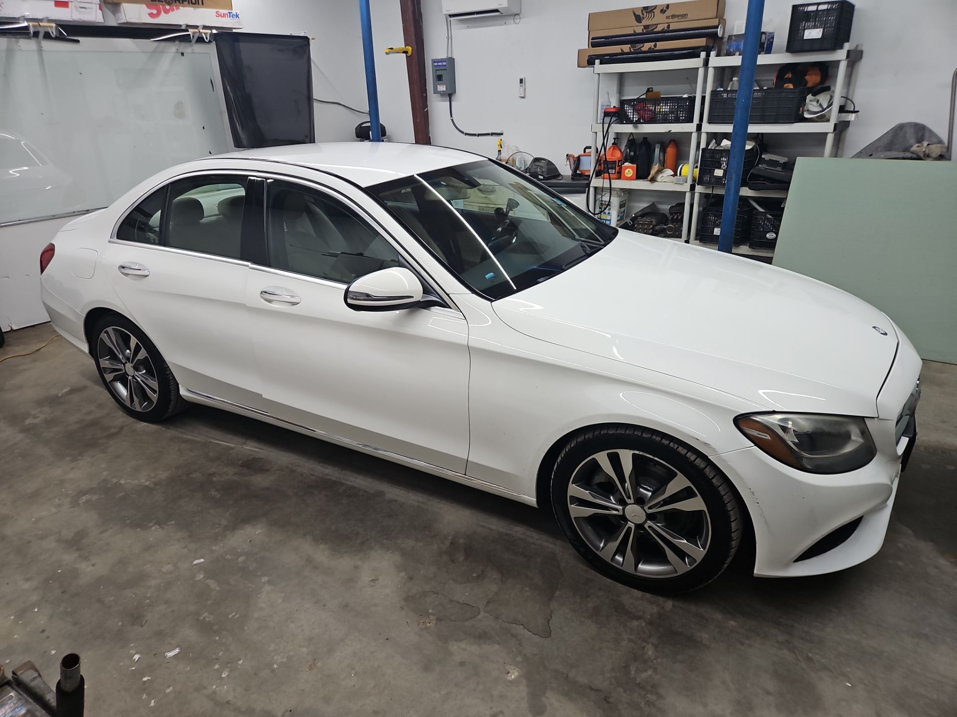 the image shows a white sedan which appears to be receiving window tinting service the technicians are likely preparing the vehicle by cleaning the windows to ensure proper adhesion of the tint film this process helps in removing any dirt or residue that may affect the final result the car's sleek design suggests that the tinting will enhance both appearance and privacy the service is being done in a professional environment indicating attention to detail and quality craftsmanship