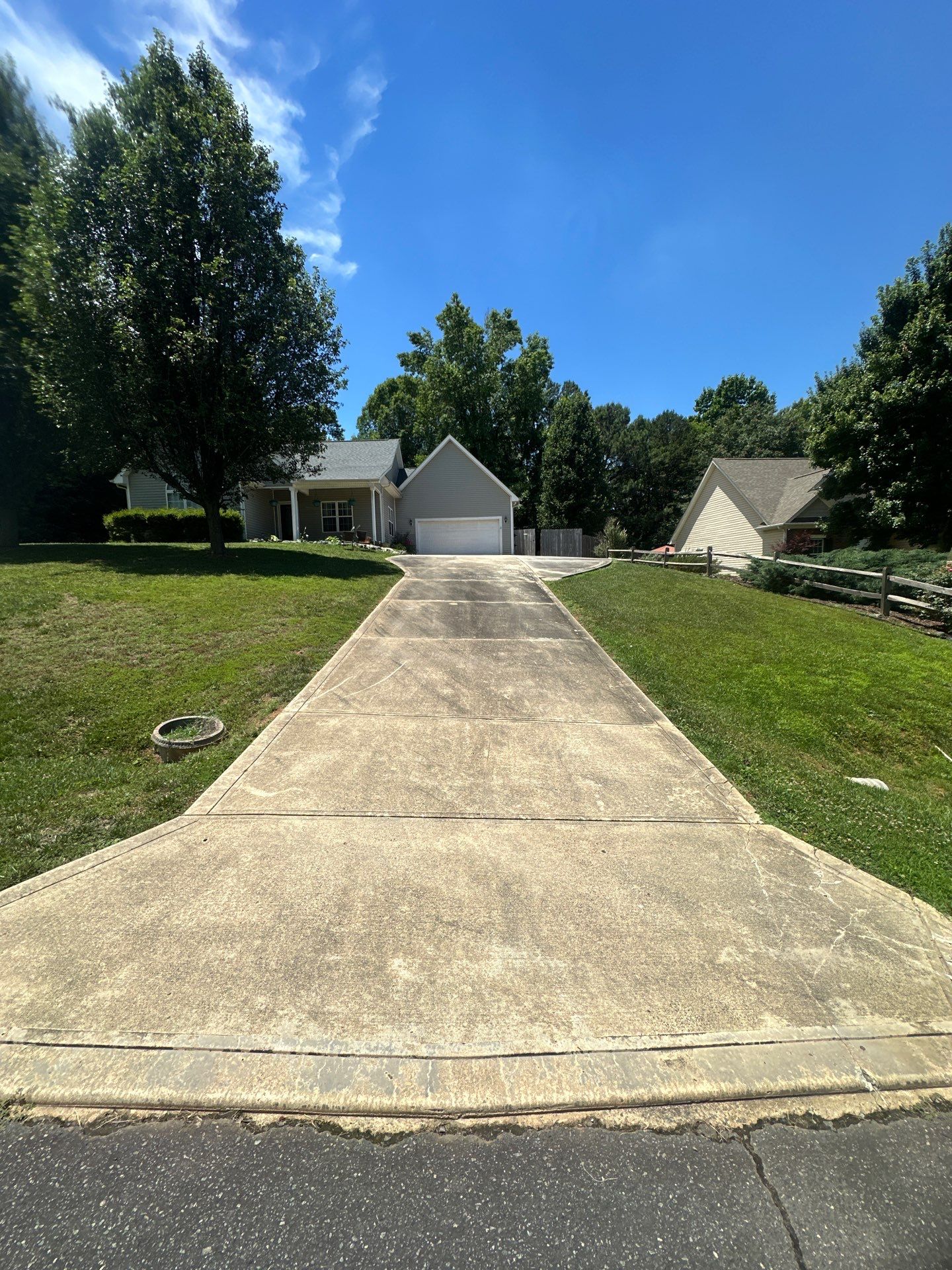 the photo shows a residential driveway leading up to a garage the surface of the driveway appears dirty and discolored indicating that it may be the subject of a pressure washing service to remove dirt grime and possibly mildew or algae common in humid climates the distinct line across the driveway suggests that one half has already been cleaned showcasing the effectiveness of the pressure washing technique which has restored the original color and cleanliness of the concrete surface the remaining half of the driveway awaits cleaning which when finished will likely match the revitalized appearance of the cleaned portion