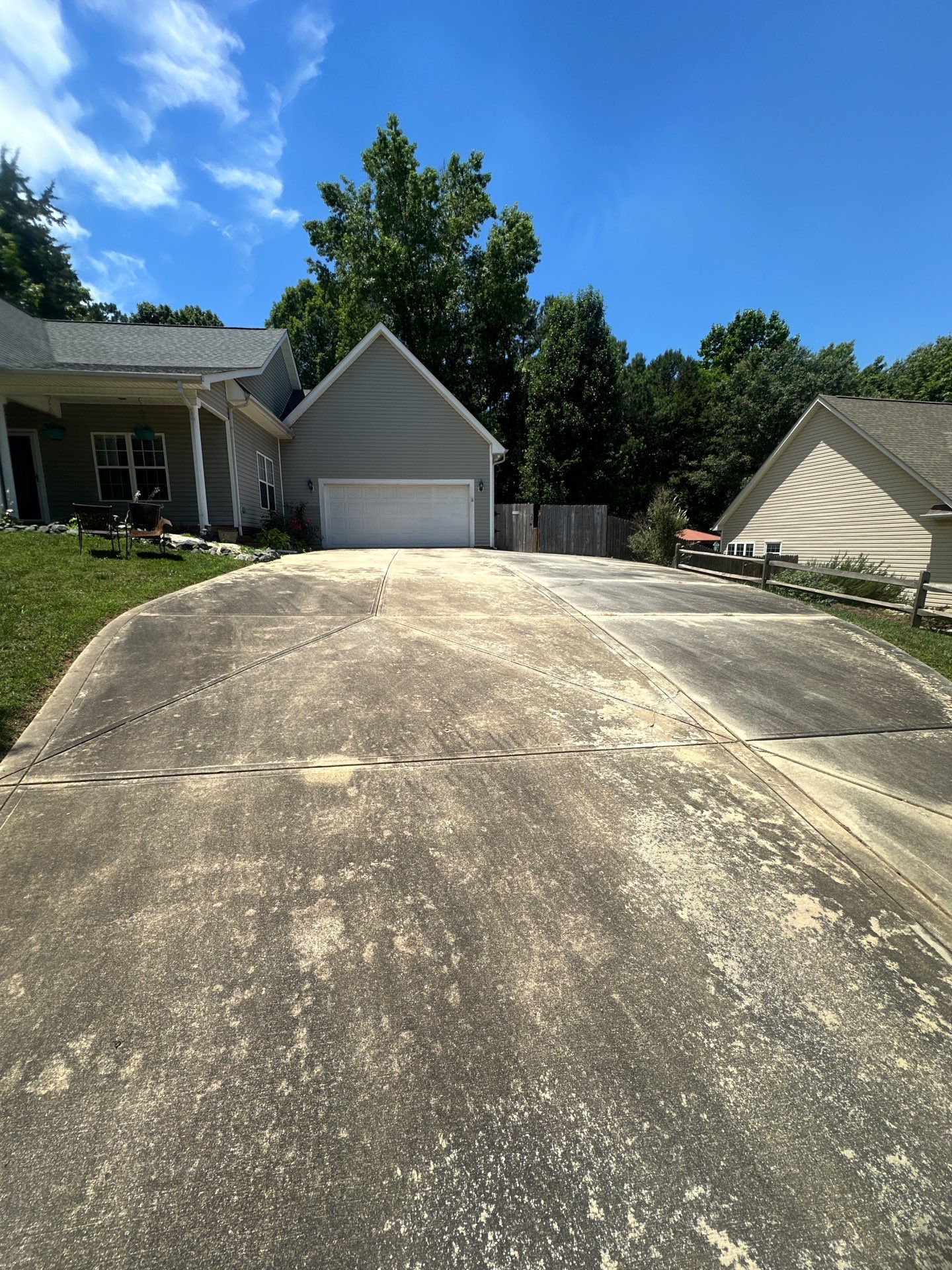 in the photo the pressure washing company is cleaning the driveway leading up to a house the driveway shows a clear distinction where the cleaning has been completed and where it has yet to be done the left side of the driveway looks much cleaner showcasing the effectiveness of the pressure washing while the right side is still covered in dirt and discoloration indicating that the job is in progress