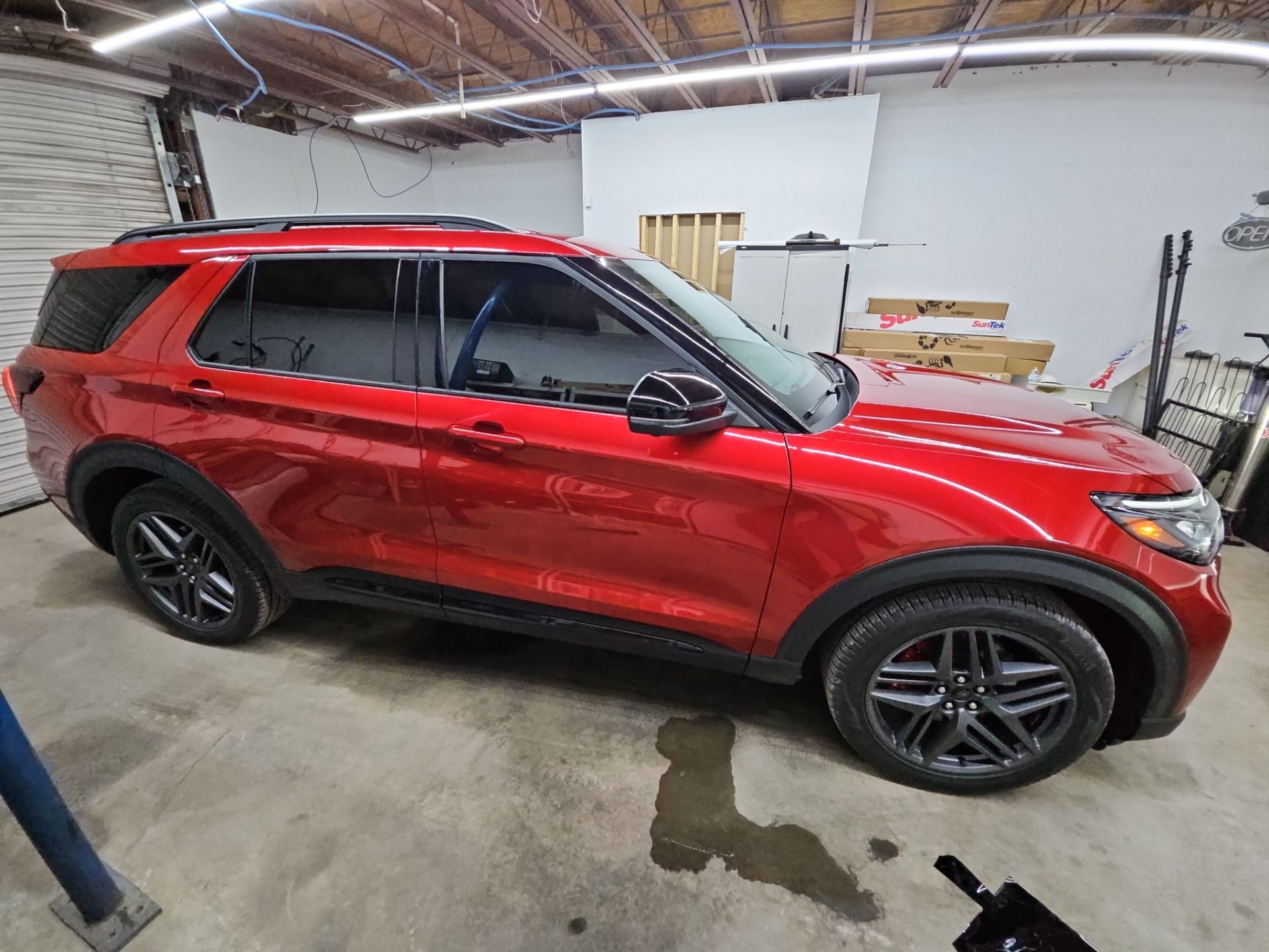 the image shows a red suv that is undergoing window tinting service at t's window tinting the vehicle is parked inside a workshop environment the windows have been tinted likely to enhance privacy and reduce heat the vehicle's shiny surface reflects the clean work area indicating attention to detail during the service the suv appears well maintained and the tinting process aims to provide both aesthetic appeal and functional benefits