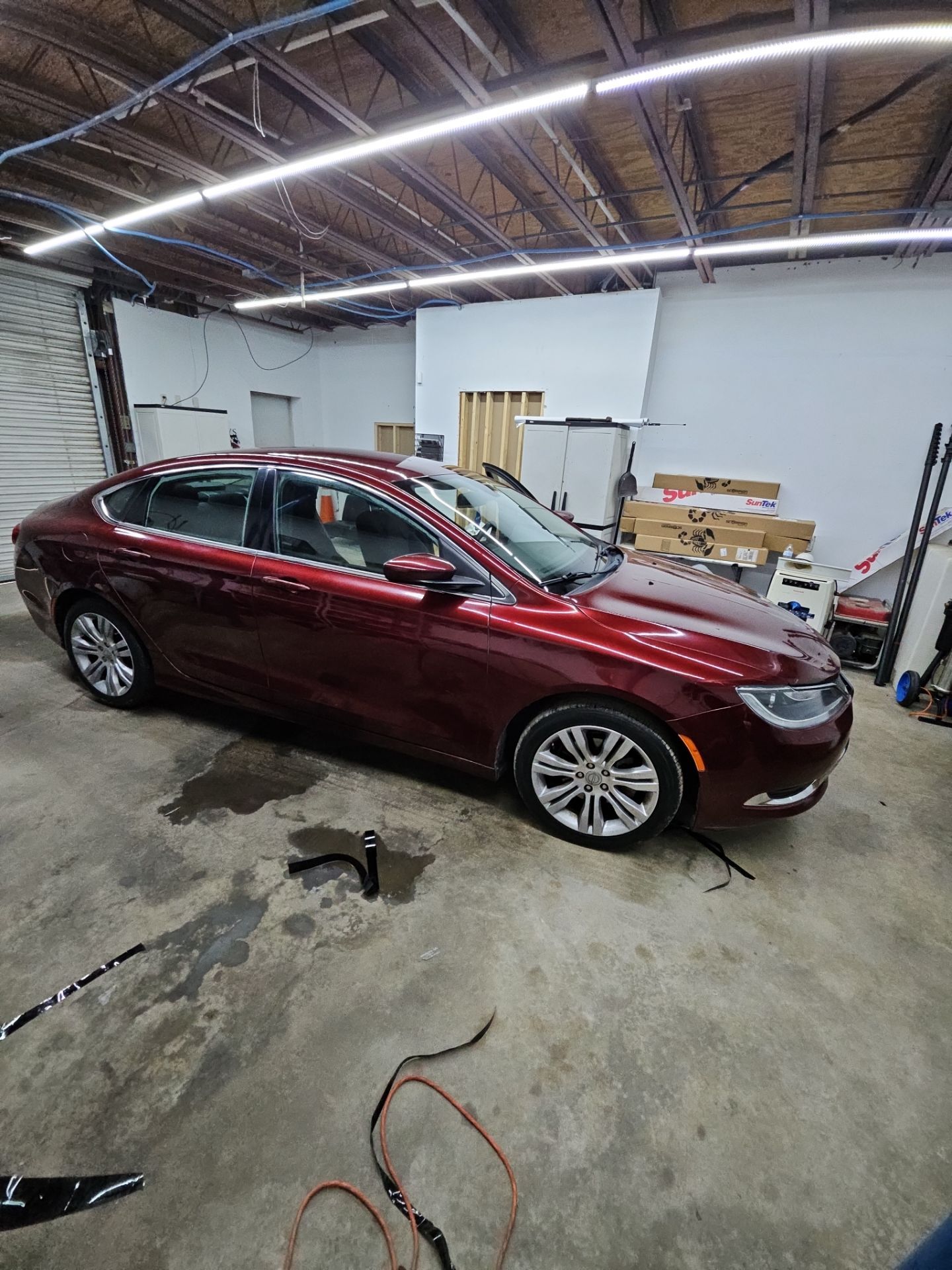 the service being done is window tinting for a red car inside a clean workshop the tint is being applied to the windows to provide privacy and reduce heat the floor shows some water and materials used for the installation the car is positioned for the technician to work efficiently on the windows