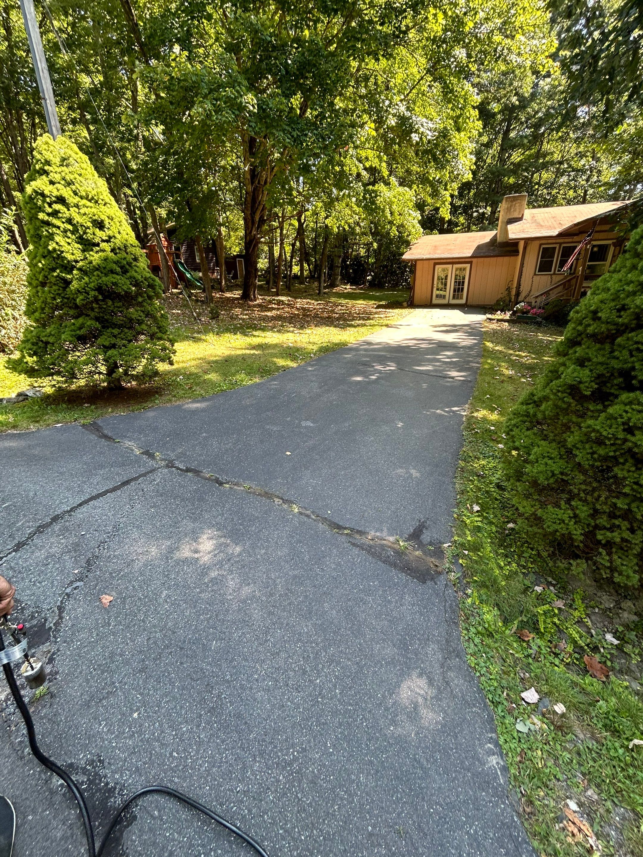 the photo shows a driveway being cleaned with a pressure washer removing dirt and debris for a refreshed appearance