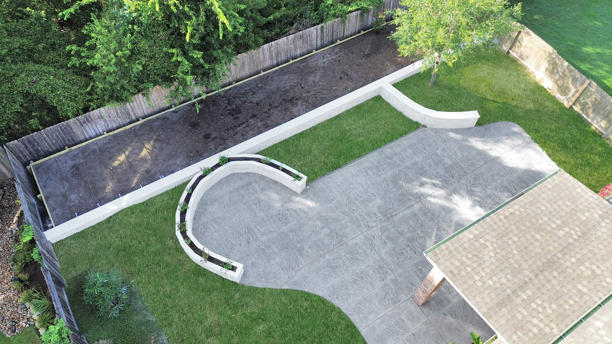 Major Transformation Project: Retaining Wall, Patio, and Drainage for Mr. & Mrs. Veerman! 🤩🛠️ We recently completed a comprehensive, custom project for Mr. & Mrs. Veerman that was all about structure, stability, and stunning outdoor design! This was a multi-phased project requiring the expertise of our Master Handcrafted Team.  Phase 1: Foundation and Water Management A successful outdoor space starts beneath the surface. We focused heavily on preparation and protection:  Demolition & Grading: We professionally removed and disposed of old dirt to achieve a level surface, ensuring the entire area was leveled and graded to enhance both appearance and functionality.  Comprehensive Drainage System: To prevent water issues and protect the new construction, we installed a complete system, connecting existing downspout gutters to channel drainage and strategically placed catch basins around the patio area.  Robust Concrete Foundation: Expert framing led to the pouring of a 4-inch deep, high PSI concrete slab to create a robust and lasting foundation for the entire retaining wall area.  Phase 2: Handcrafted Structure and Style This phase brought in our masonry and carpentry artisans to build the defining elements of the new space:  Custom Retaining Wall: Our master handcrafted team built a stunning, structural retaining wall. This involved careful framing, precise concrete work, and meticulous masonry construction with vertical supports every 3 feet for maximum stability.  Client Involvement: Mr. & Mrs. Veerman played a key role in selecting the retainer wall fascia and stone materials, ensuring the final look perfectly matched their vision.  Stamped Concrete Patio: We installed a beautiful stamped concrete patio. This decorative concrete work involved imprinting a pattern into the fresh concrete, giving them the high-end look of stone or brick with the durability of concrete.  Walk Add-On: Extended the stamped concrete to include a new, seamless walk area.  (Optional) Custom Garden Box: Constructed durable, raised garden boxes using 2"x12" boards and strong 4"x6" posts.  Phase 3: Landscaping and Finishing Touches The final details bring the entire project to life, focusing on irrigation and planting:  Sprinkler System Upgrade: To support their new landscaping, we upgraded their irrigation system by installing two new drip zones and a new control unit.  Flower Beds: Integrated new flower beds along the retaining wall and patio, ready for planting.  Decoration: Concluded the project with personalized decoration options to perfectly complement their beautiful, newly structured space.  Thinking About a Multi-Layered Outdoor Project? This project demonstrates our ability to seamlessly handle complex jobs—from heavy-duty drainage and structural construction to decorative finishes and irrigation.  The proposed timeline for this extensive project was 10 to 15 working days!  ❓ Do you have a sloping yard or drainage issues that could be solved with a functional and beautiful retaining wall? Tell us your challenge! 👇  💡 We specialize in bringing intricate outdoor visions to life! If you're looking for a team with master craftsmen for your next patio, retaining wall, or full landscape overhaul, let's talk. by Texas Urban Elements