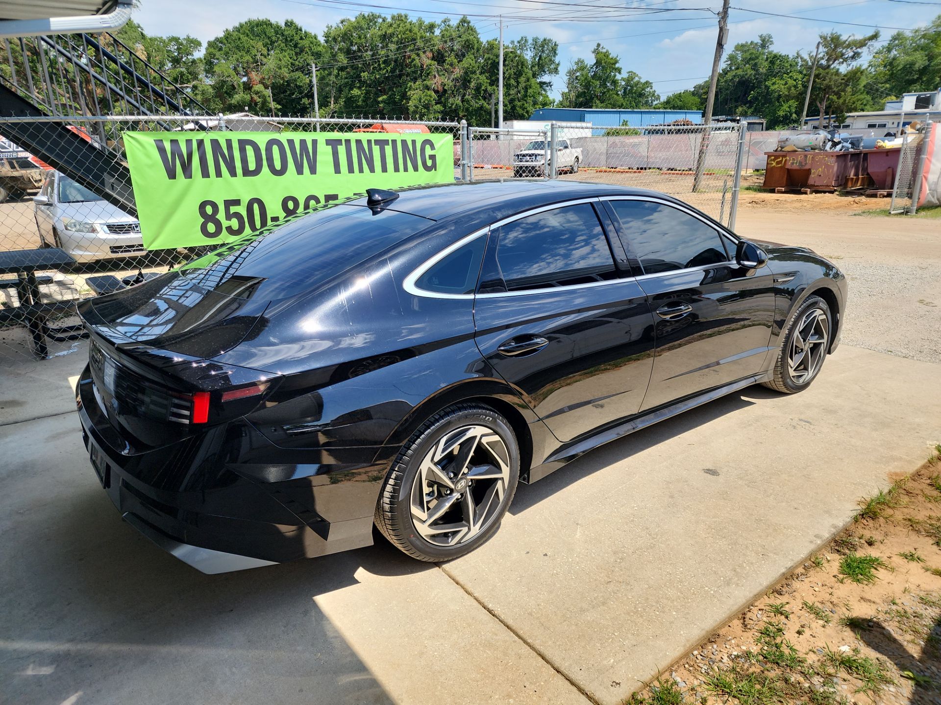 the car shown in the photo is parked outside a business that specializes in window tinting the photo features a black sedan with freshly applied window tints on all side windows and the rear window the tinting service provides added privacy and uv protection for the vehicle's passengers and interior the car appears to be in a lot designated for customers awaiting or having completed the tinting service