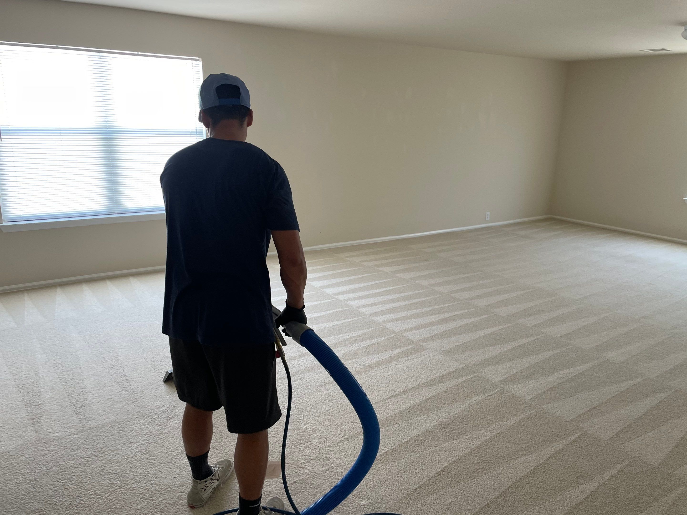 carpet cleaning being performed on a large beige carpet in an empty room with natural light