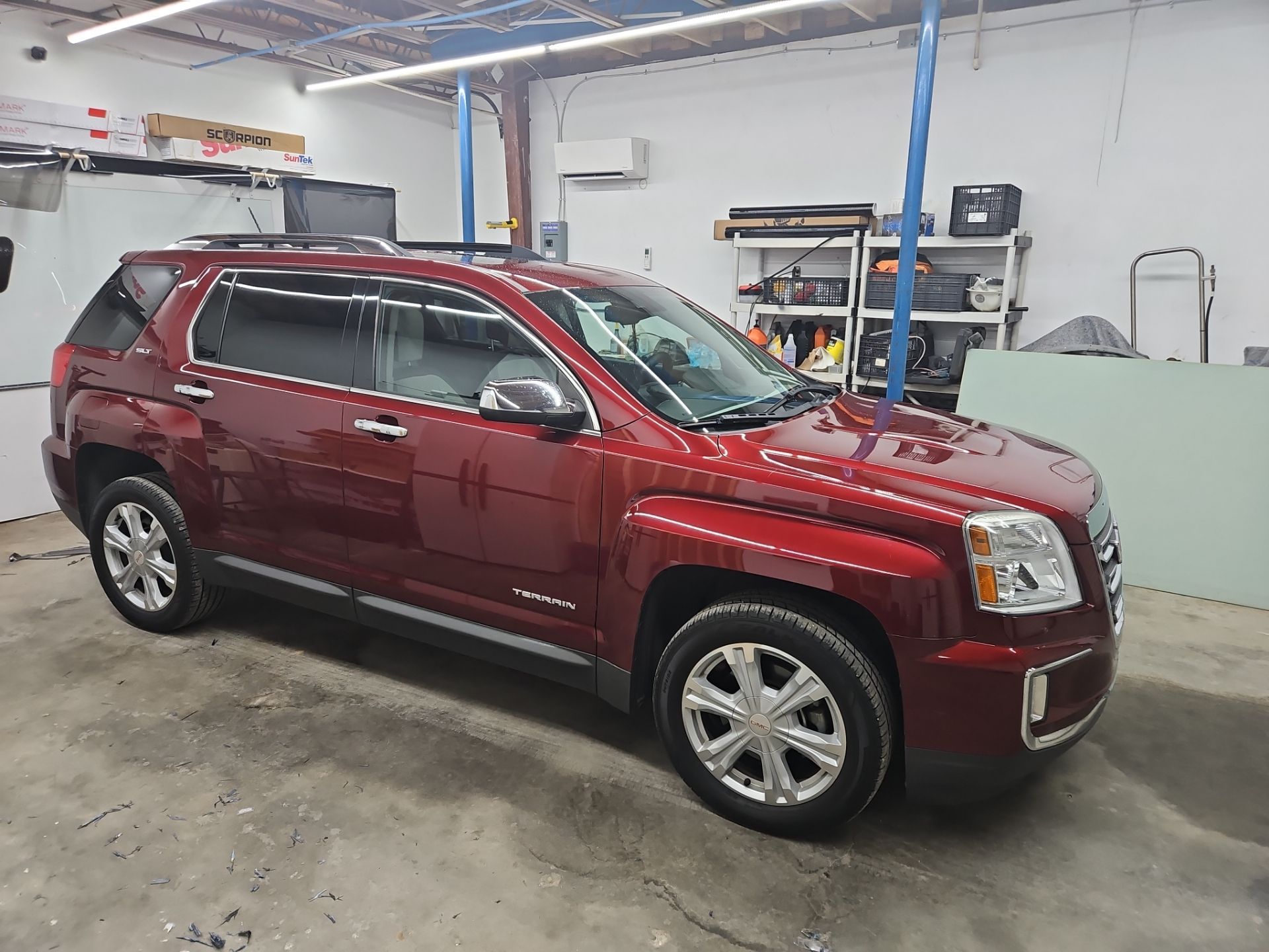 this image shows a red suv inside a workshop with the company specializing in window tinting work being done on the vehicle the windows appear to have dark tints applied to them the service being performed is the process of applying a film to the windows to reduce glare offer privacy and block harmful uv rays this can enhance the vehicle's appearance and provide comfort for the occupants