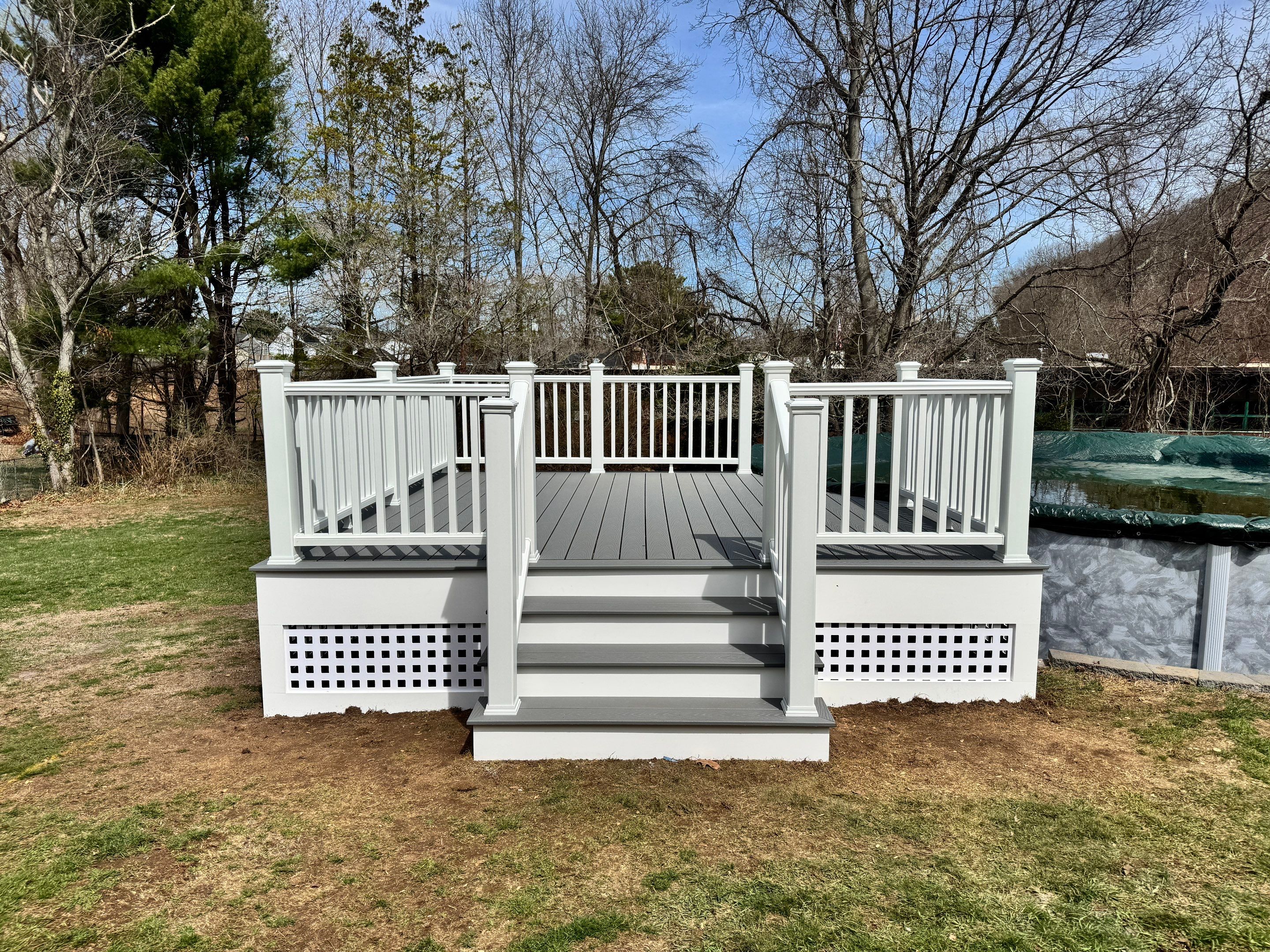New pool deck using Trex Pebble Gray boards and White composite railings and lattice  by DiGiorgi Roofing and Siding Inc