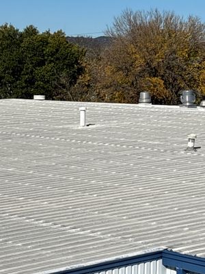 Metal roof with white vent pipe and trees
