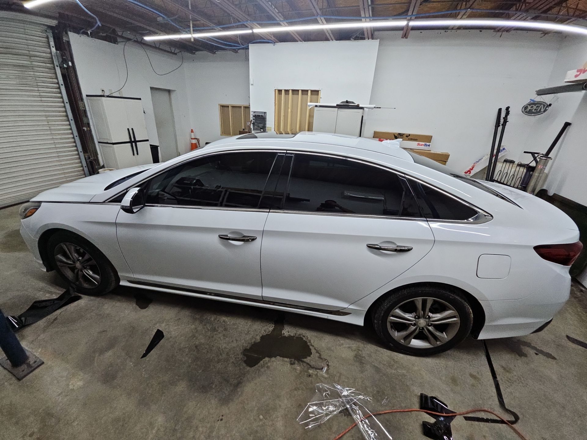 the service being done is window tinting on a white car the tint is likely being applied to the side and rear windows the process involves cutting and fitting tint film to the glass to reduce glare and heat inside the vehicle this improves the car's appearance and provides privacy the work area is a clean garage with tools and materials visible indicating a professional service