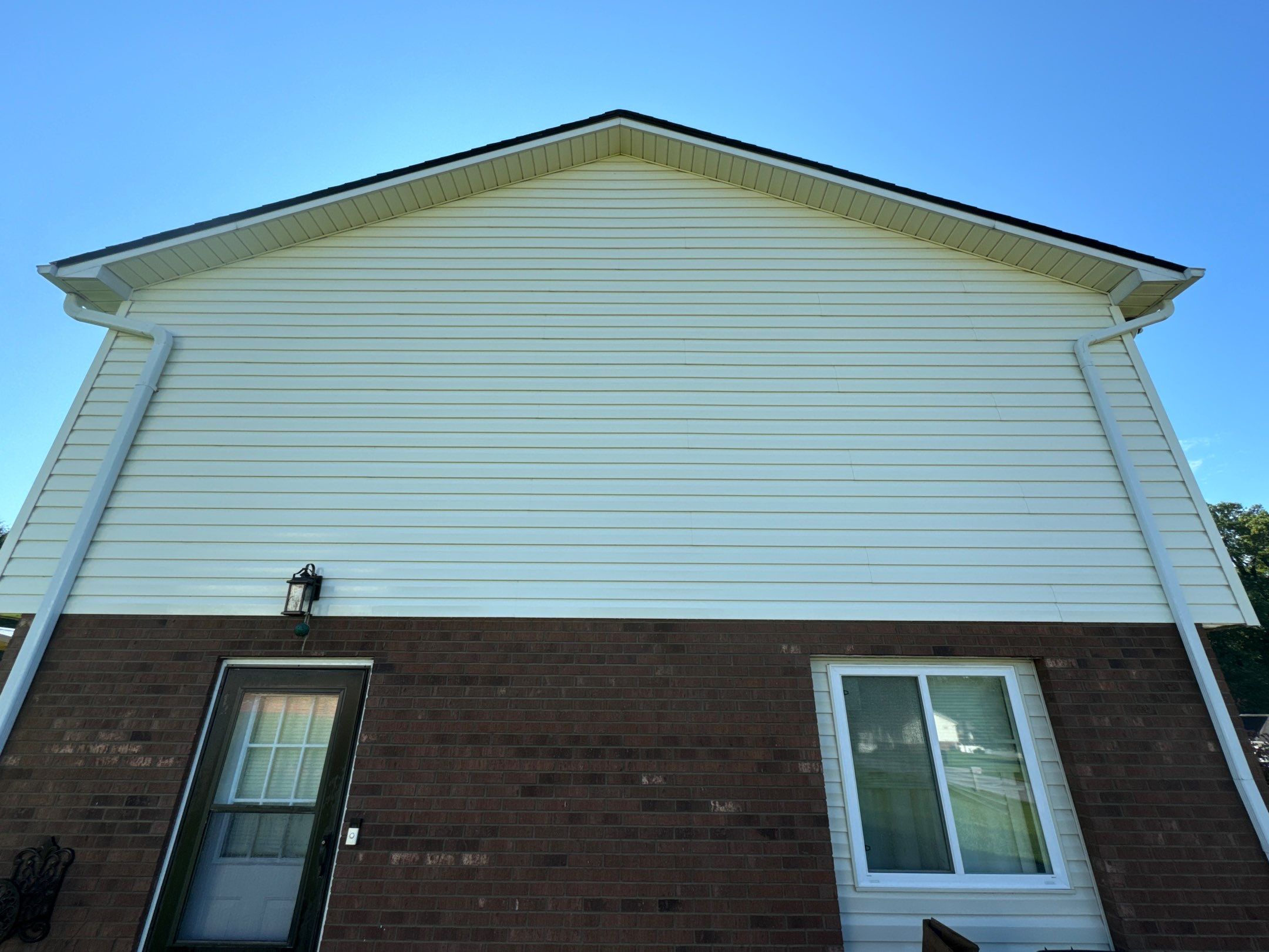 the service shown is cleaning the vinyl siding and brick surface of a house using pressure washing techniques