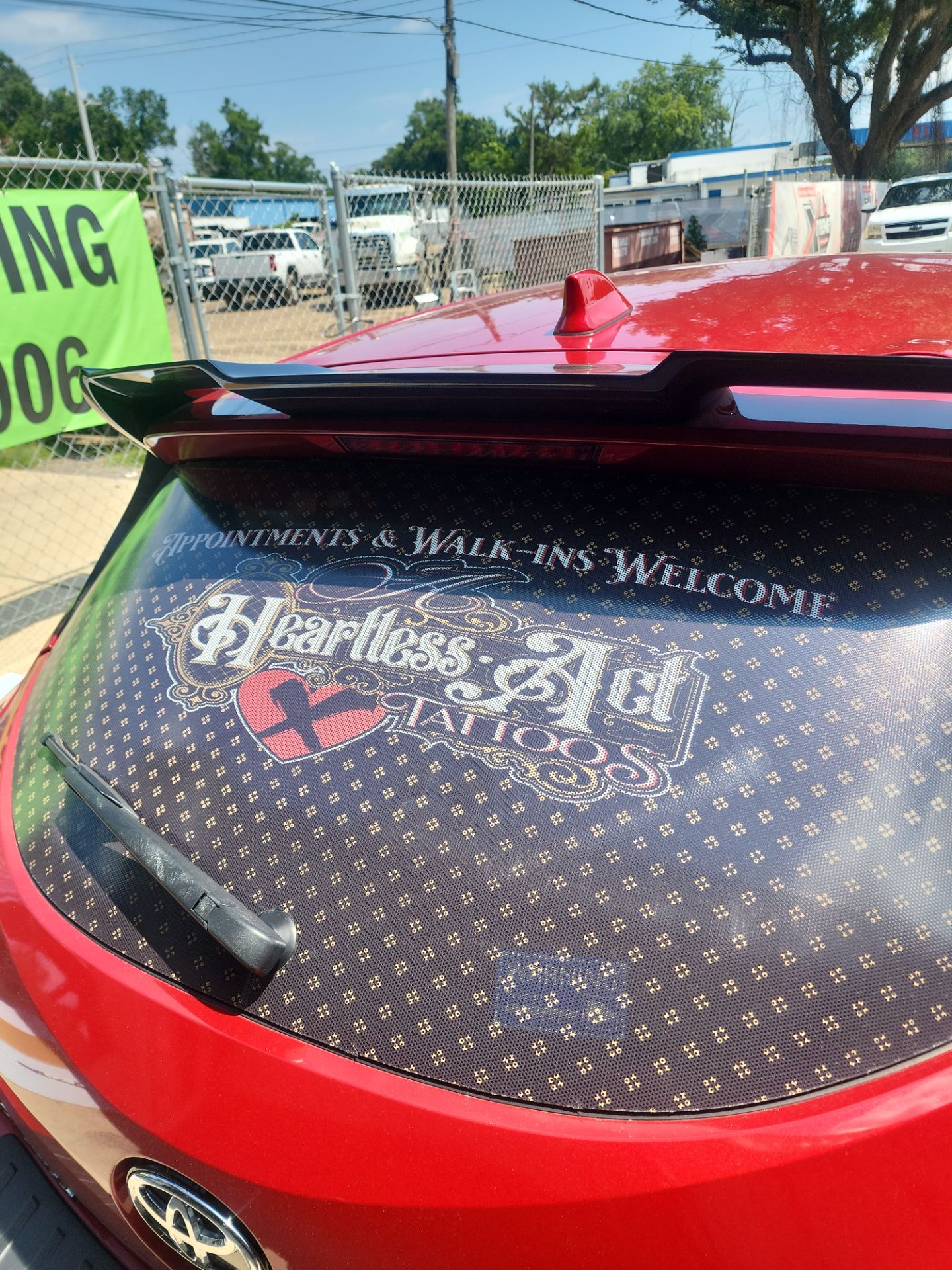 a window tinting company named t's window tinting based in pensacola fl is providing a service on a red car the service involves applying a custom vinyl or tint with printed advertisements on the rear window of the car the tint includes graphics and text promoting a tattoo shop