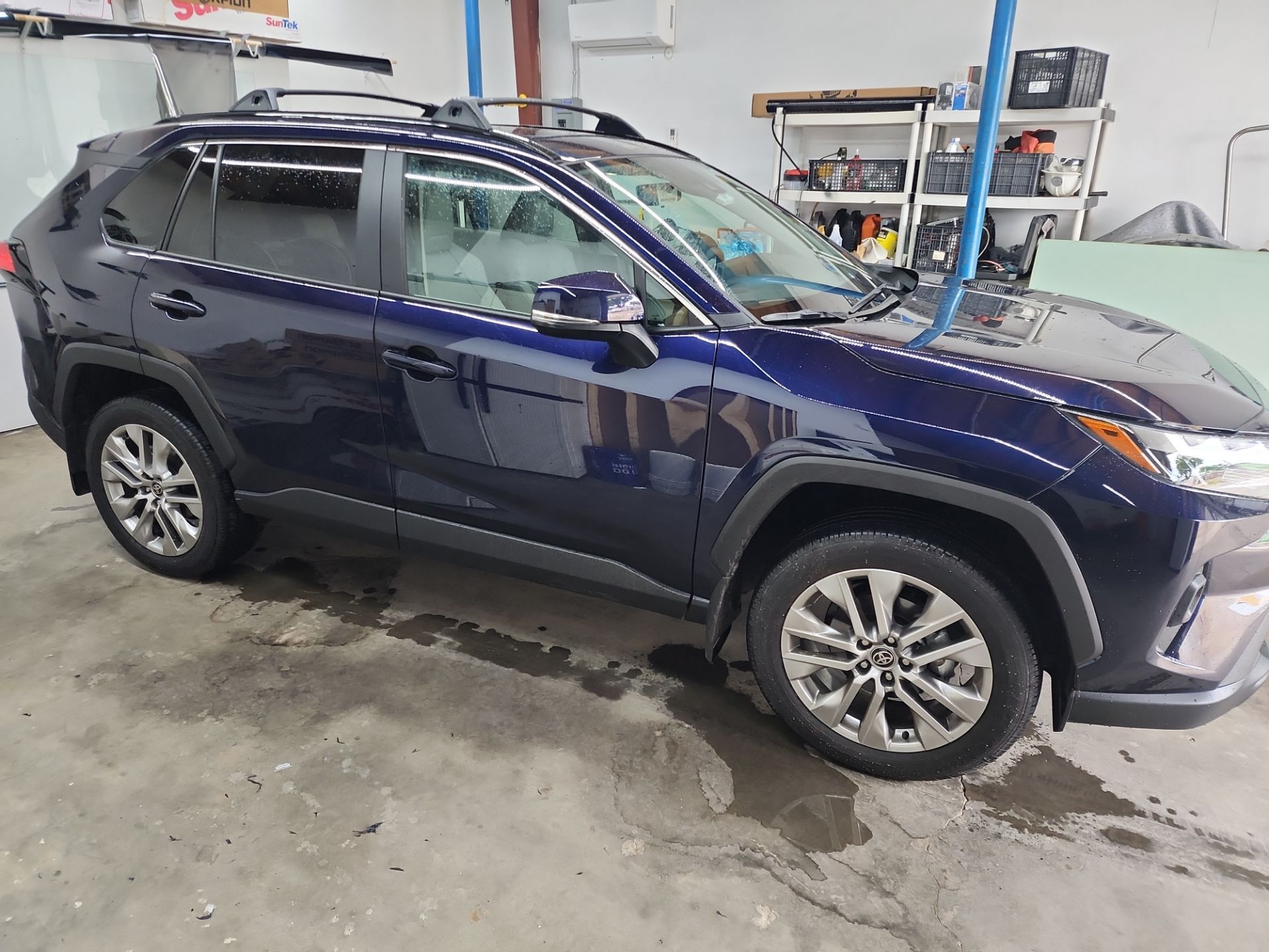 a window tinting company named t's window tinting based in pensacola fl is applying window tint film to a blue suv the car is parked inside a garage and the workers are in the process of installing the tint on the windows you can see some of the tools and materials used for the tinting process in the background