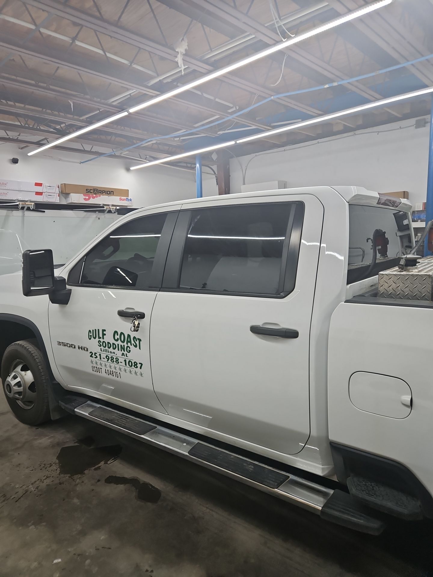 the window tinting company is applying window film to the side windows of a white pickup truck this service enhances privacy reduces glare and protects the interior from uv rays the installation process involves cleaning the windows cutting the film to size and carefully applying it to ensure a smooth finish the truck appears to be undergoing professional tint installation indoors in a workshop