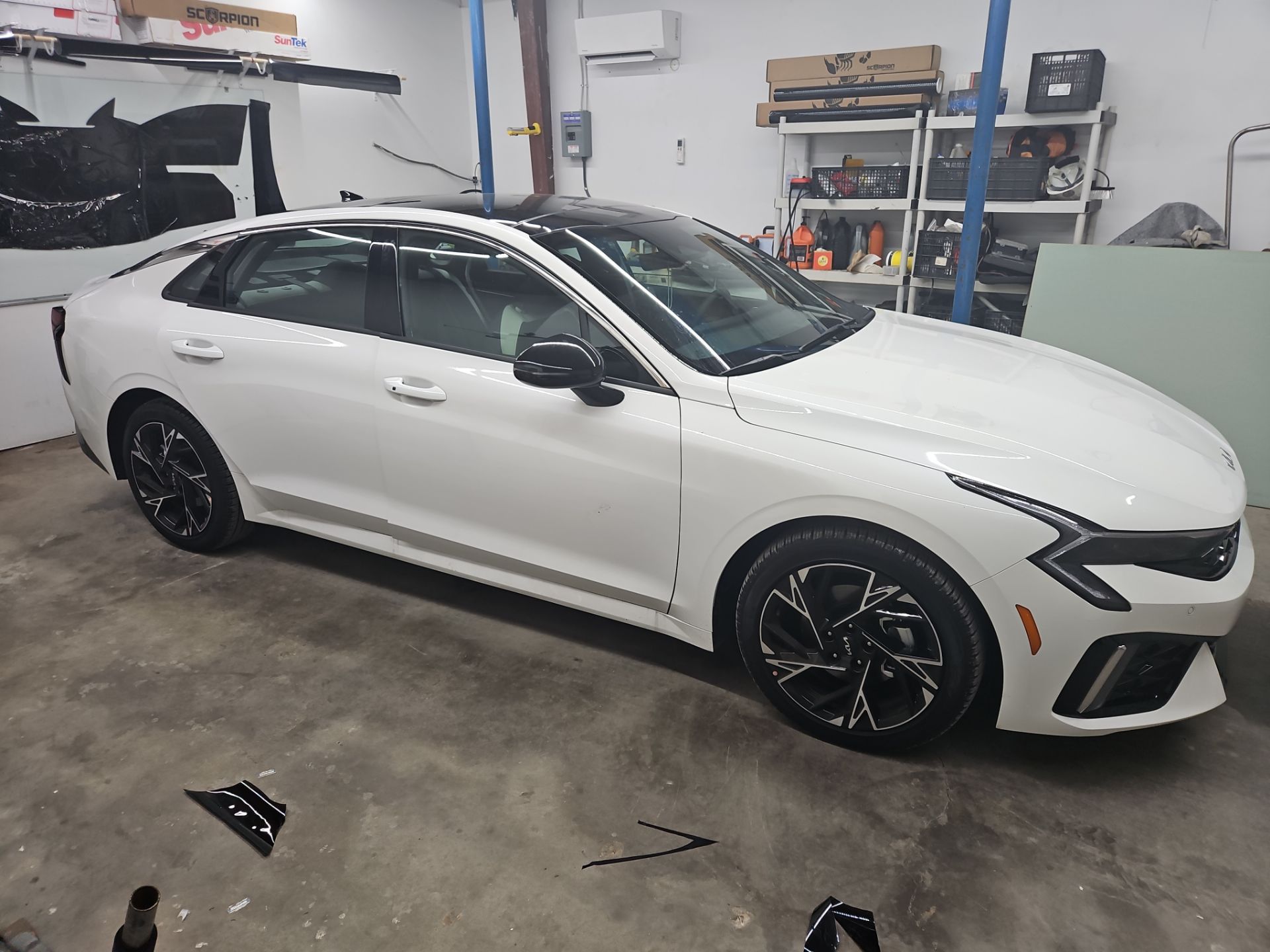 the service being done is window tinting on a newer model sedan the car has a sleek white exterior and black accents the tinting appears to be applied to the side and back windows to enhance privacy and reduce heat inside the vehicle the setting suggests a professional environment focused on precise installation the overall finish will improve the look and functionality of the car while providing added comfort to the occupants