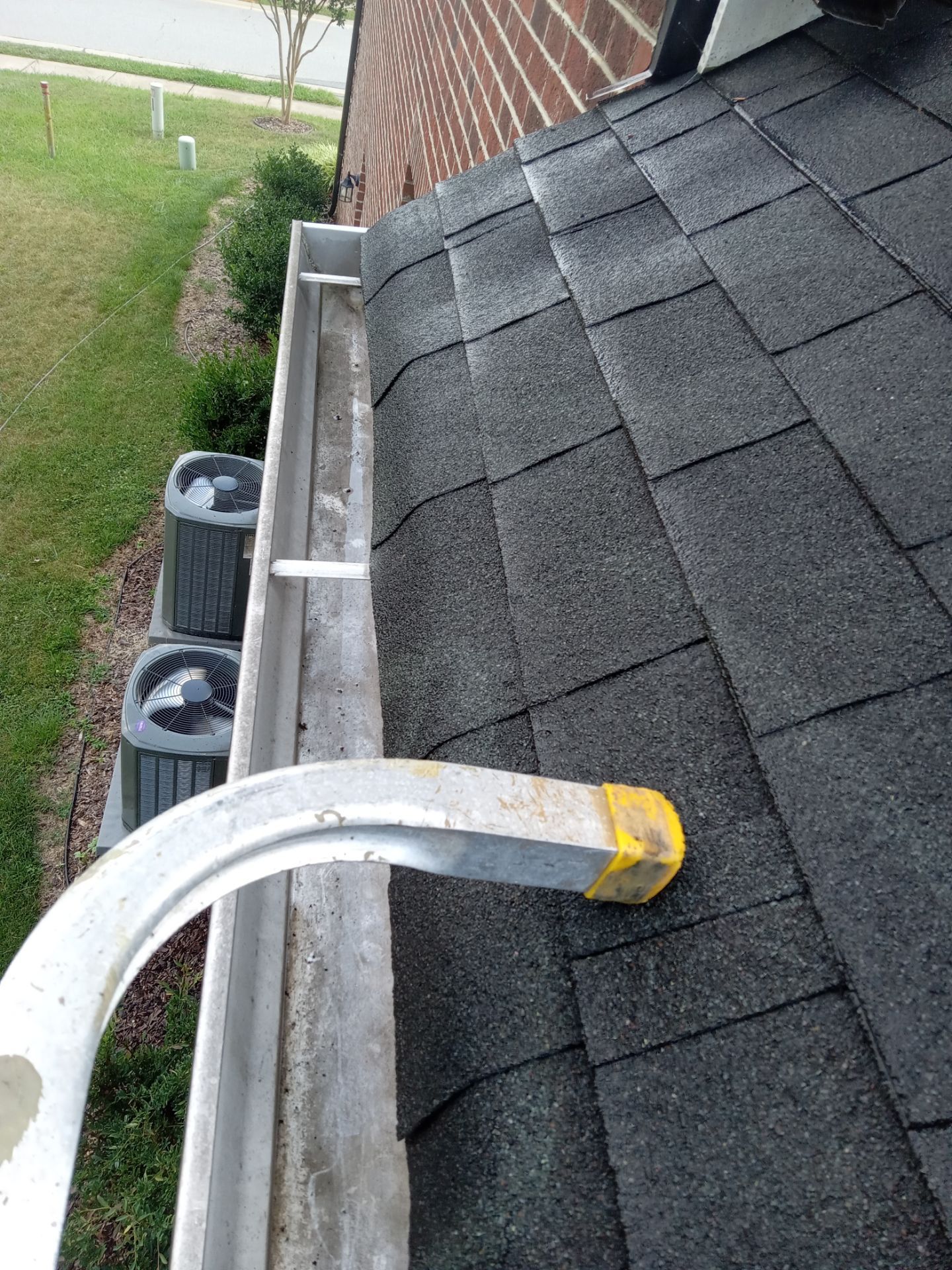 gutter cleaning removing debris buildup in gutters on a residential house roof using manual tools no pressure washing equipment visible