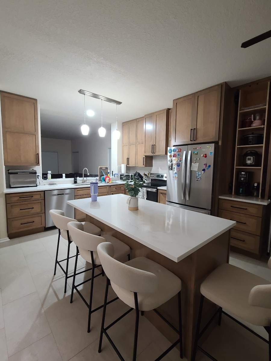The old kitchen had a traditional builder-grade look with heavier wood cabinetry and busier finishes, while the new kitchen has a warm transitional design with cleaner lines, a brighter palette, and a more open, modern layout by Mena stone surfaces