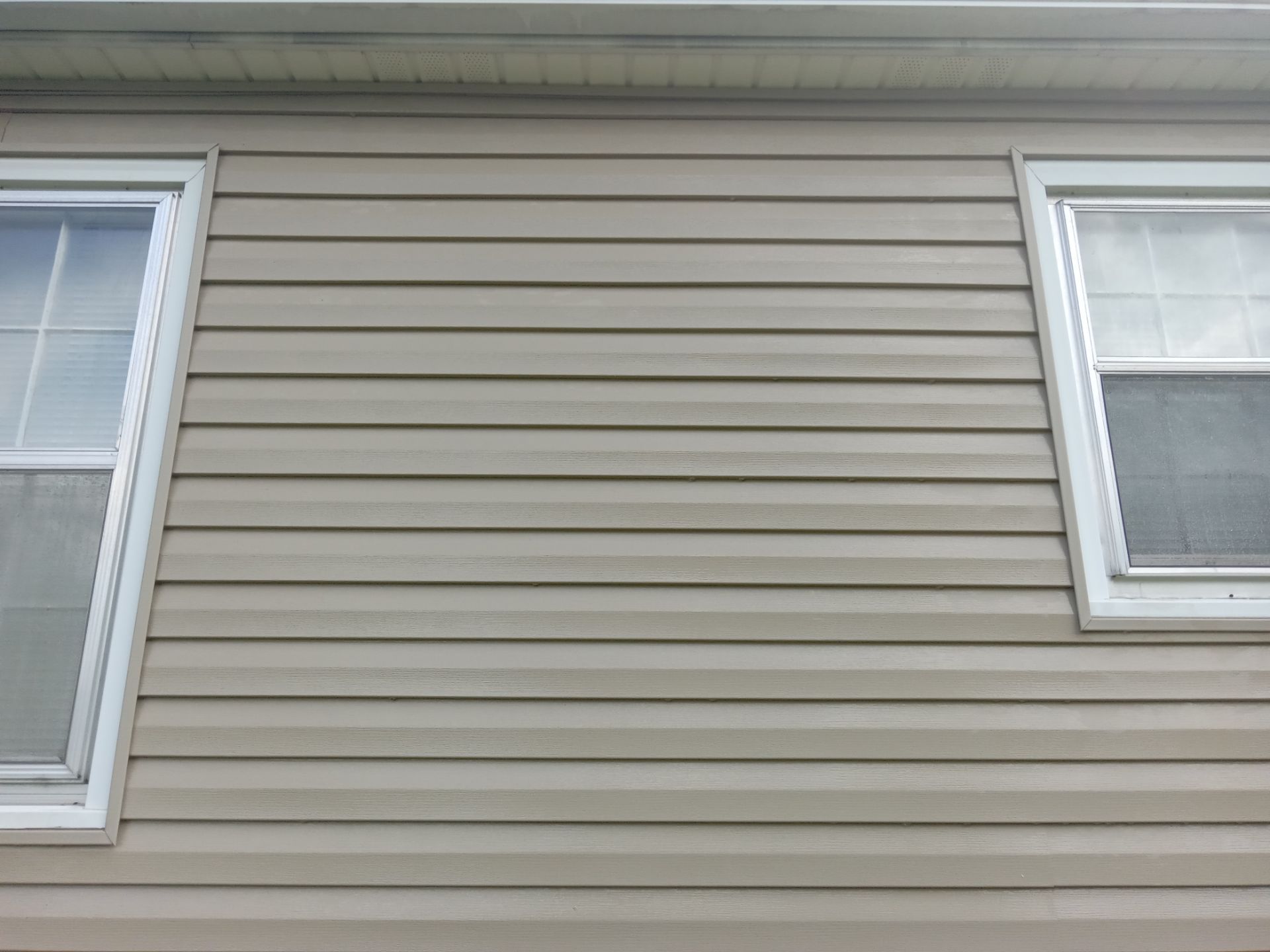 in the photo a pressure washing company is cleaning the exterior siding of a house the siding is likely made of vinyl or a similar material and the pressure washing is done to remove dirt grime and possibly mildew or algae buildup to restore the appearance of the siding the service may also involve cleaning around the windows and the eaves to ensure a complete and clean look for the house exterior