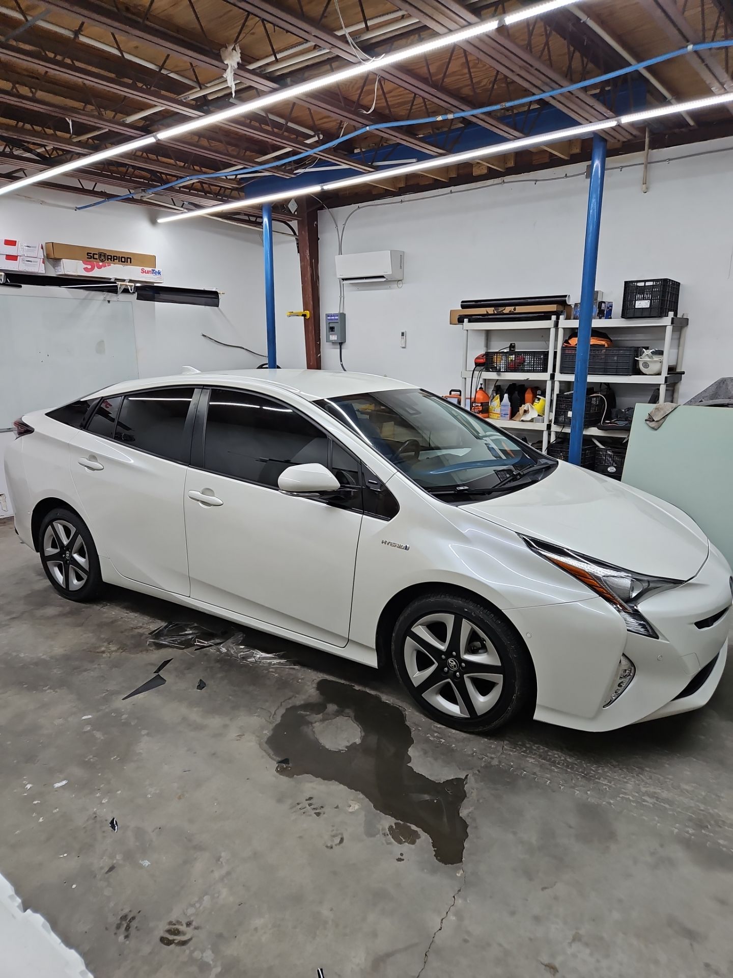 the photo shows a white toyota prius parked indoors indicating it is receiving window tinting services the windows are likely being treated with a film that reduces heat and glare while enhancing privacy the clean and organized workspace suggests a professional approach to the installation process overall it appears to be a routine tint application for better comfort and aesthetics