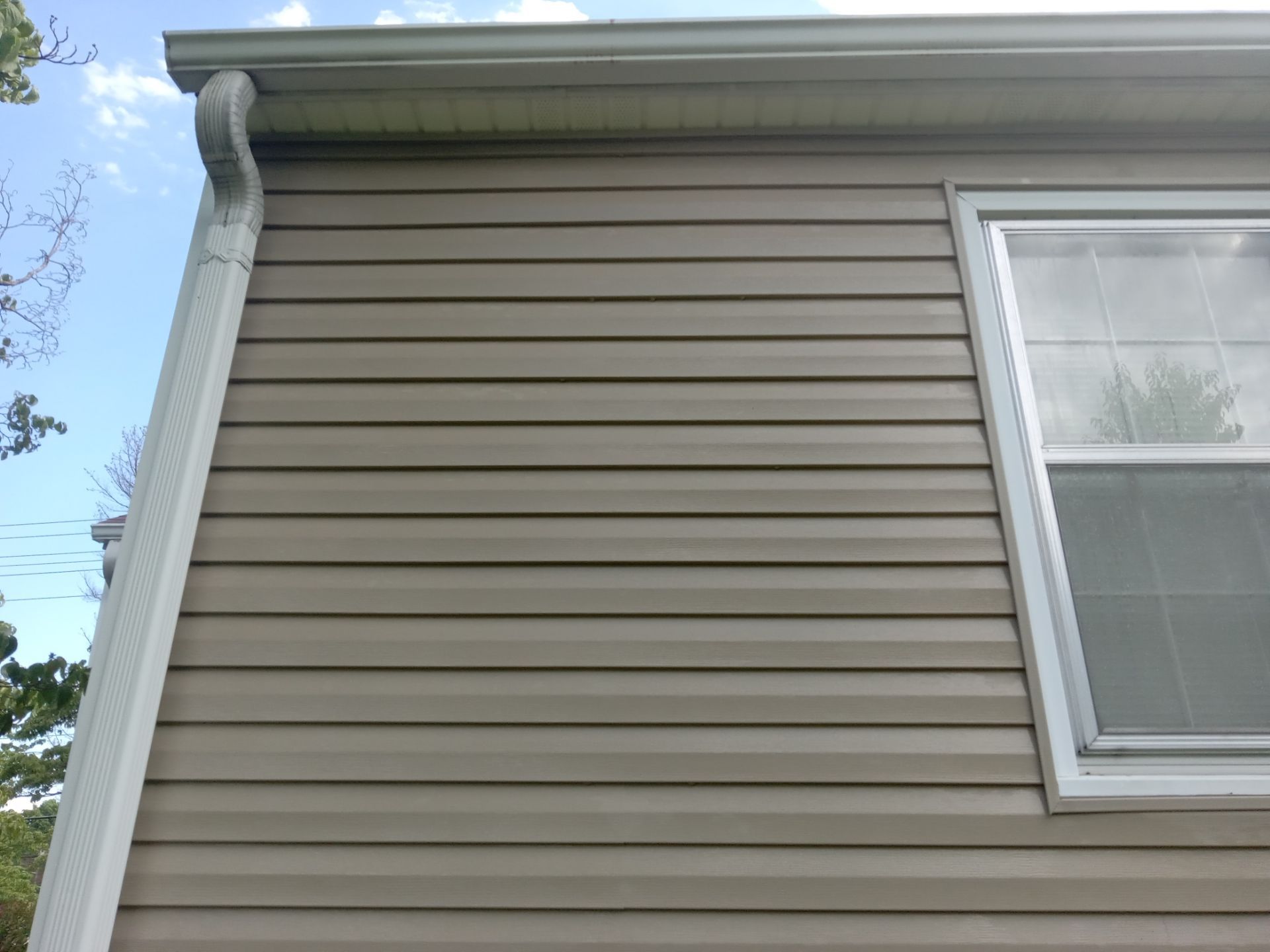 the photo shows the side of a house with vinyl siding being cleaned by a pressure washing company the service includes cleaning the exterior siding of the house to remove dirt, grime, and possibly mildew or algae buildup typical for houses in areas with humidity and variable weather the pressure washing is also likely to be aimed at the gutters and downspouts as they too can collect debris and stains over time the service helps to maintain the aesthetic of the home and can also prevent long term damage caused by the buildup of unwanted substances on the exterior surfaces