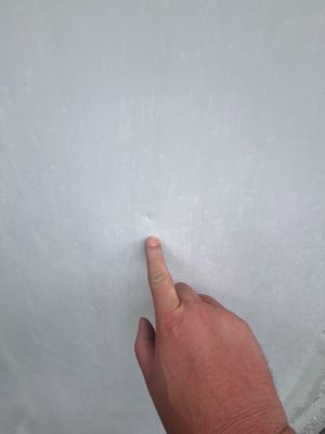 Hand pointing to small dent on metal roof panel