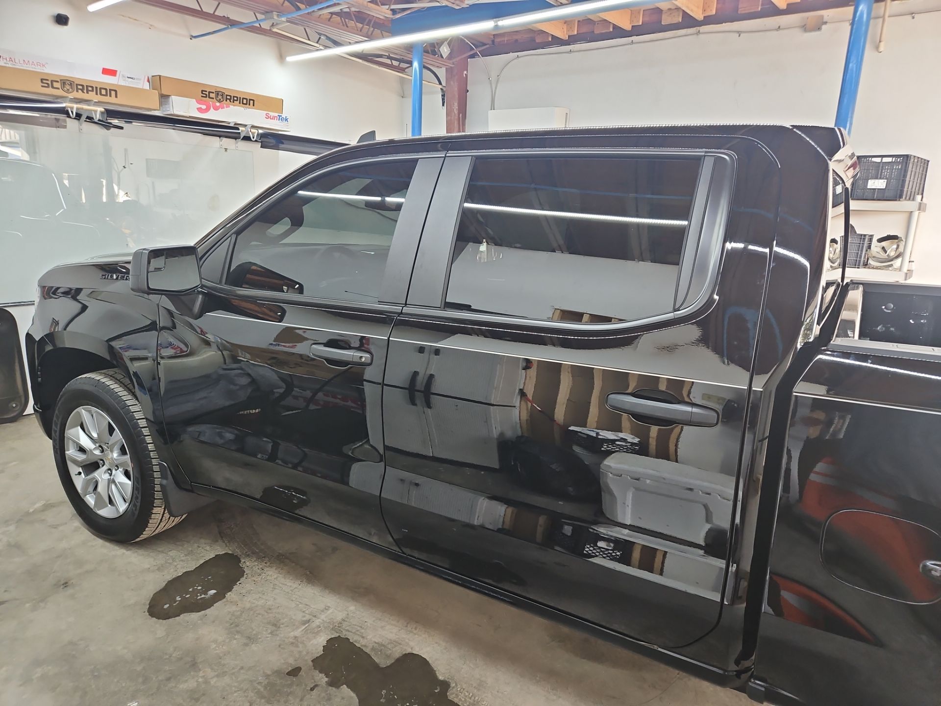 the image shows a black pickup truck that is likely undergoing a window tinting service the windows appear to be clean and prepped for the application of window film the tinting process will enhance privacy reduce glare and improve the overall aesthetic of the vehicle the shop seems well organized with tools and materials readily available for the job