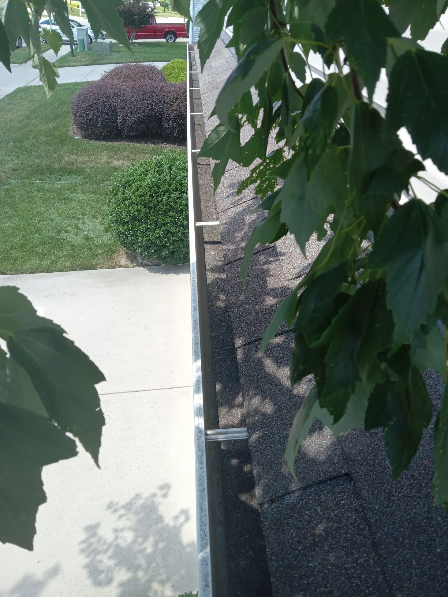 the image shows a concrete sidewalk and part of a roof where the surface color variance indicates pressure washing is in progress or was recently completed the visible part of the sidewalk closest is clean and appears to have been recently washed compared to the farther section which looks darker and likely still dirty the roof also shows a clear line between a cleaner section and a part with darker shingles indicating a cleaning service has been or is being performed to remove dirt moss or other buildup using high pressure water jets