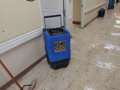 Blue R340 drying equipment placed along a hallway with reflective tile flooring.