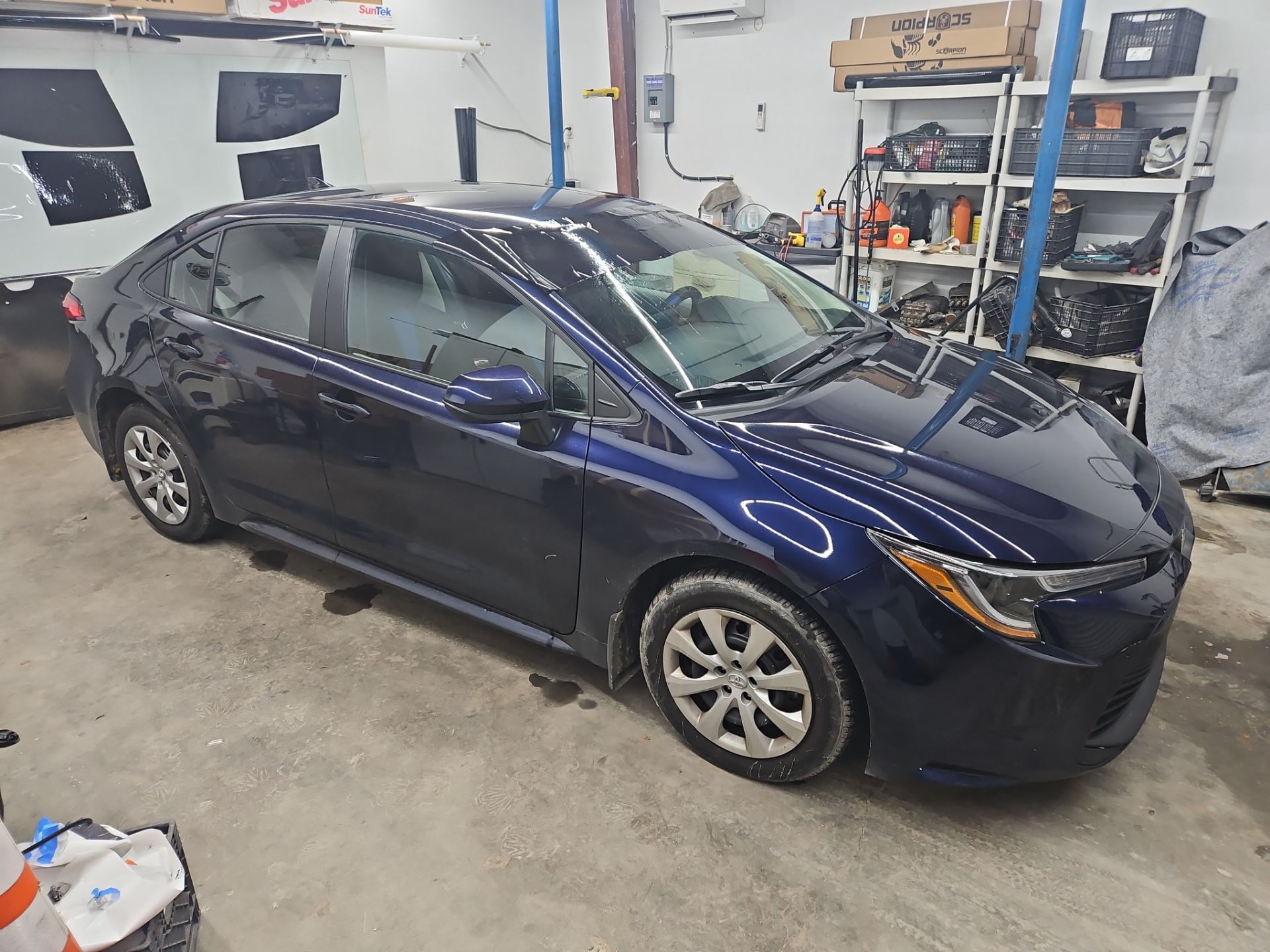 the service being done in the photo is window tinting on a dark blue sedan the company is applying a film to the windows which helps reduce glare and heat while providing privacy the car is securely positioned in a shop environment where the technicians can work efficiently the tinting will enhance the vehicle's appearance and improve comfort for passengers