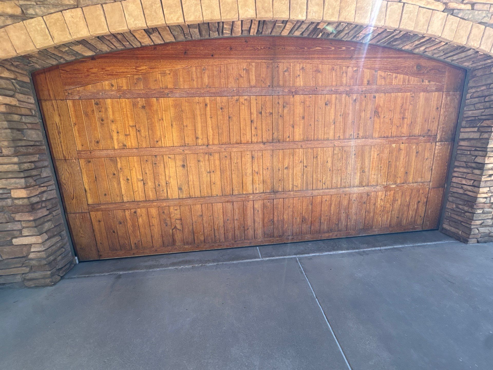 Existing stained wood garage door with a stone surround, photographed for the Colorado Springs restoration estimate