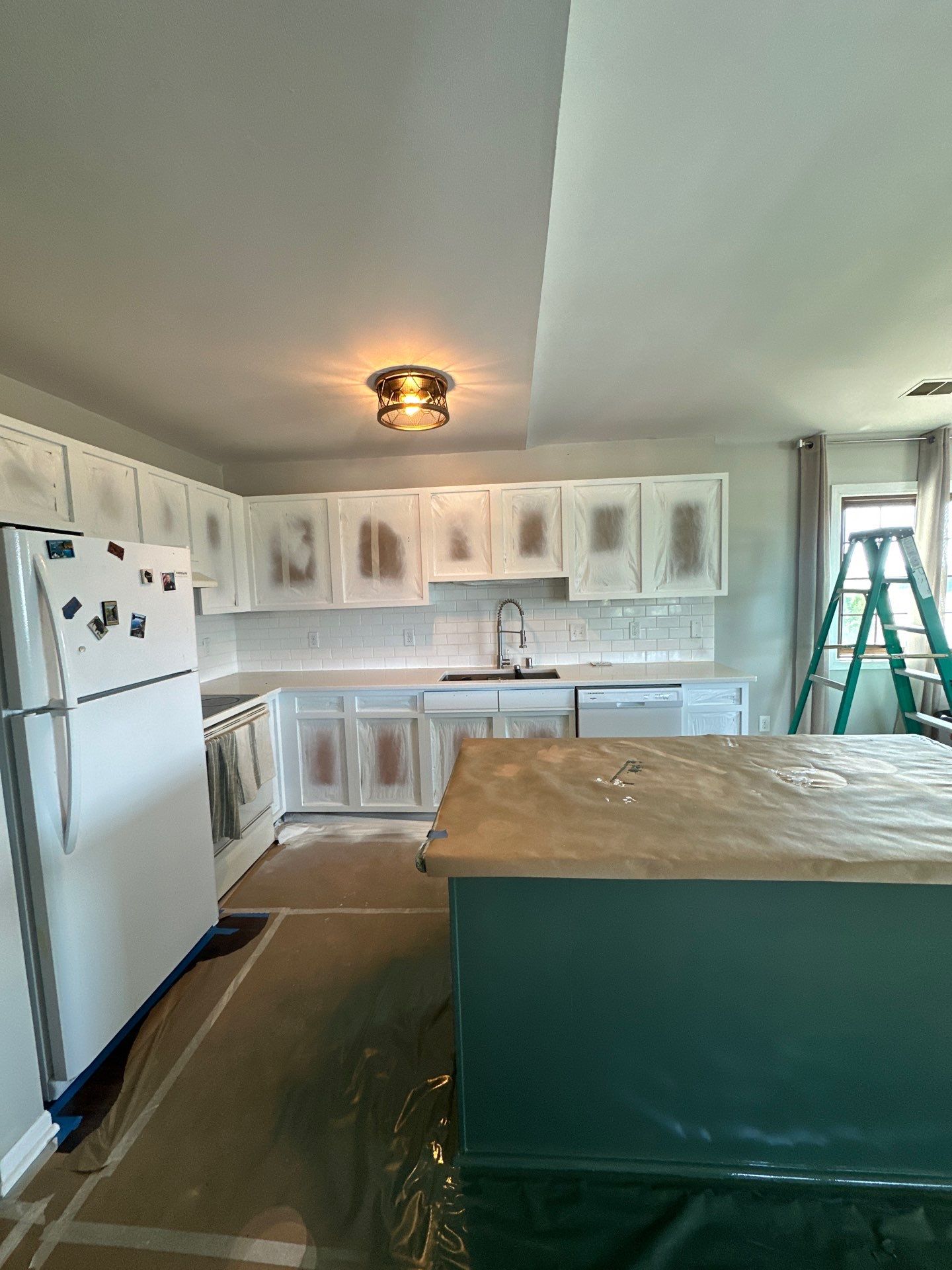 Kenosha kitchen with cabinet openings masked, counters covered, and floors protected during refinishing
