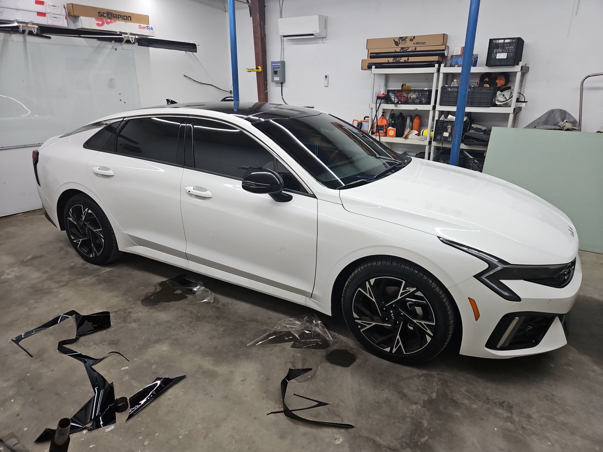 the service being done is window tinting on a white car the technicians are applying dark window film to the side and rear windows the area is clean with tools and leftover tinting material on the floor the tint helps reduce heat and glare while providing privacy and style to the vehicle the car appears to be in a professional shop setting dedicated to car enhancements